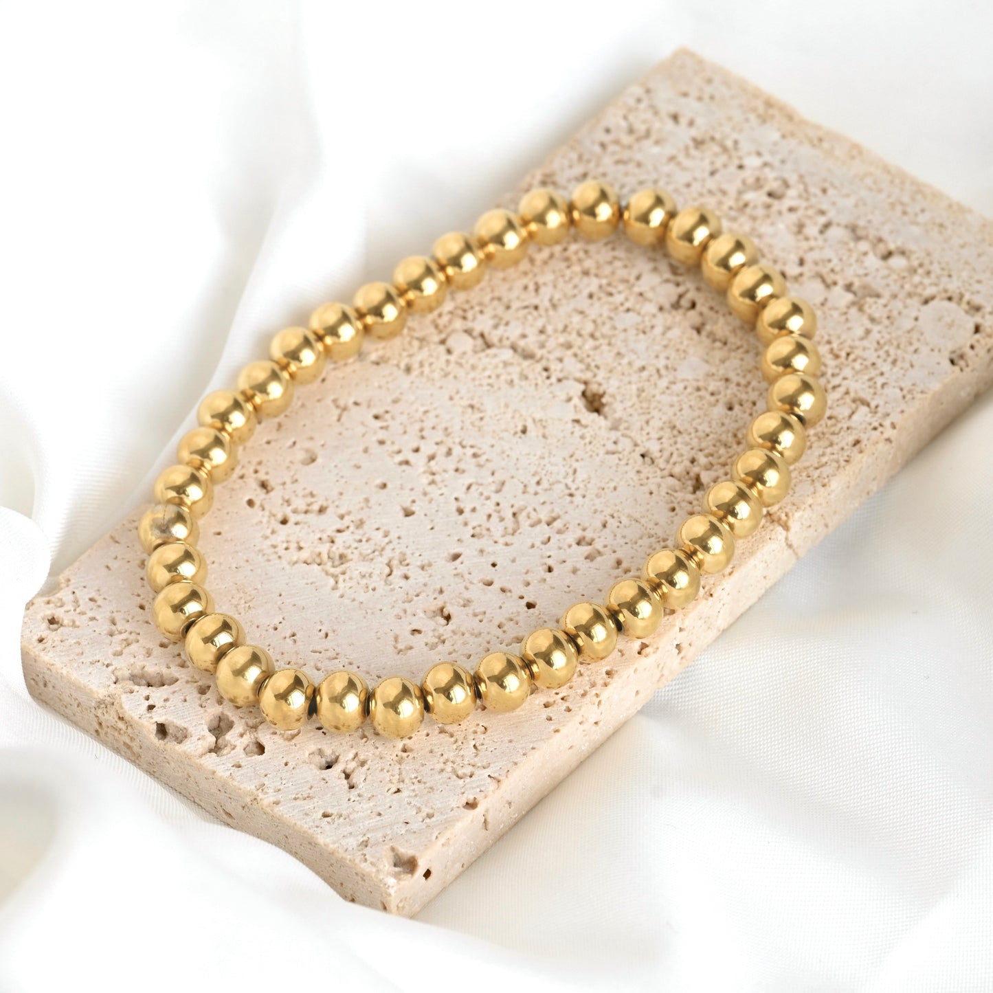 Gold beaded stretch bracelet on a textured stone surface