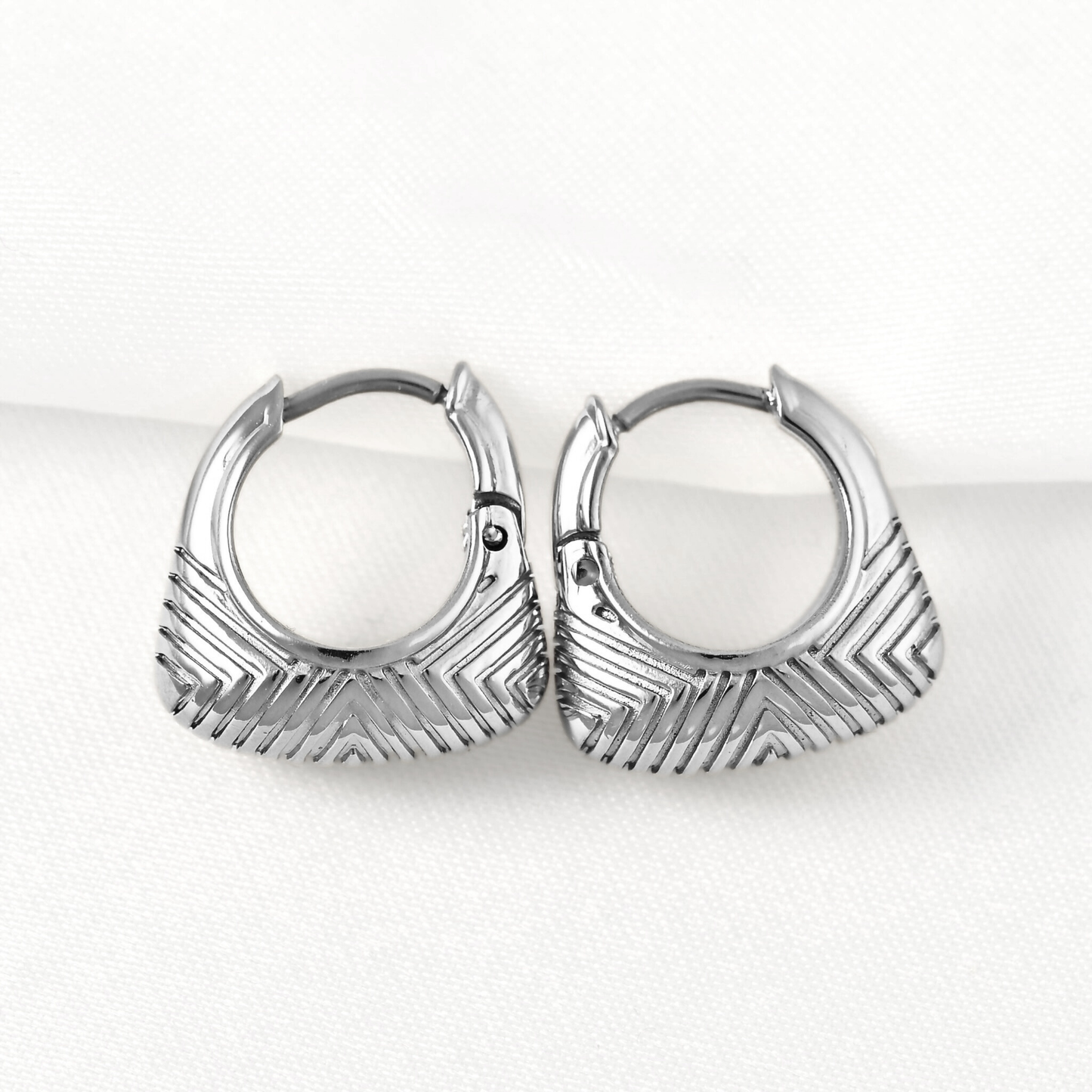A pair of silver-toned hoop earrings with a textured chevron pattern, displayed on a clean white background.