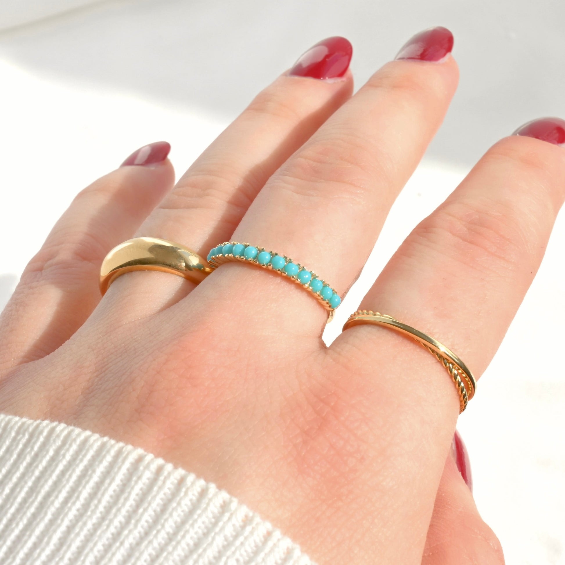 Hand wearing gold turquoise gemstone ring stacked with a dainty twisted and chunky dome rings in gold on a white background