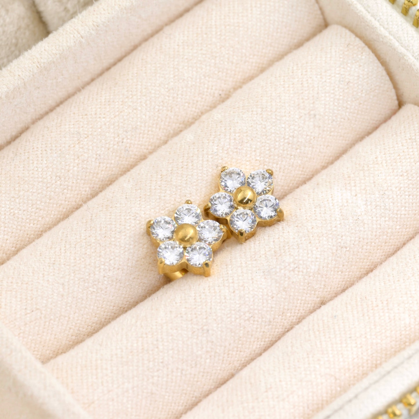 Small gold flower earrings with diamonds in a beige jewelry display tray