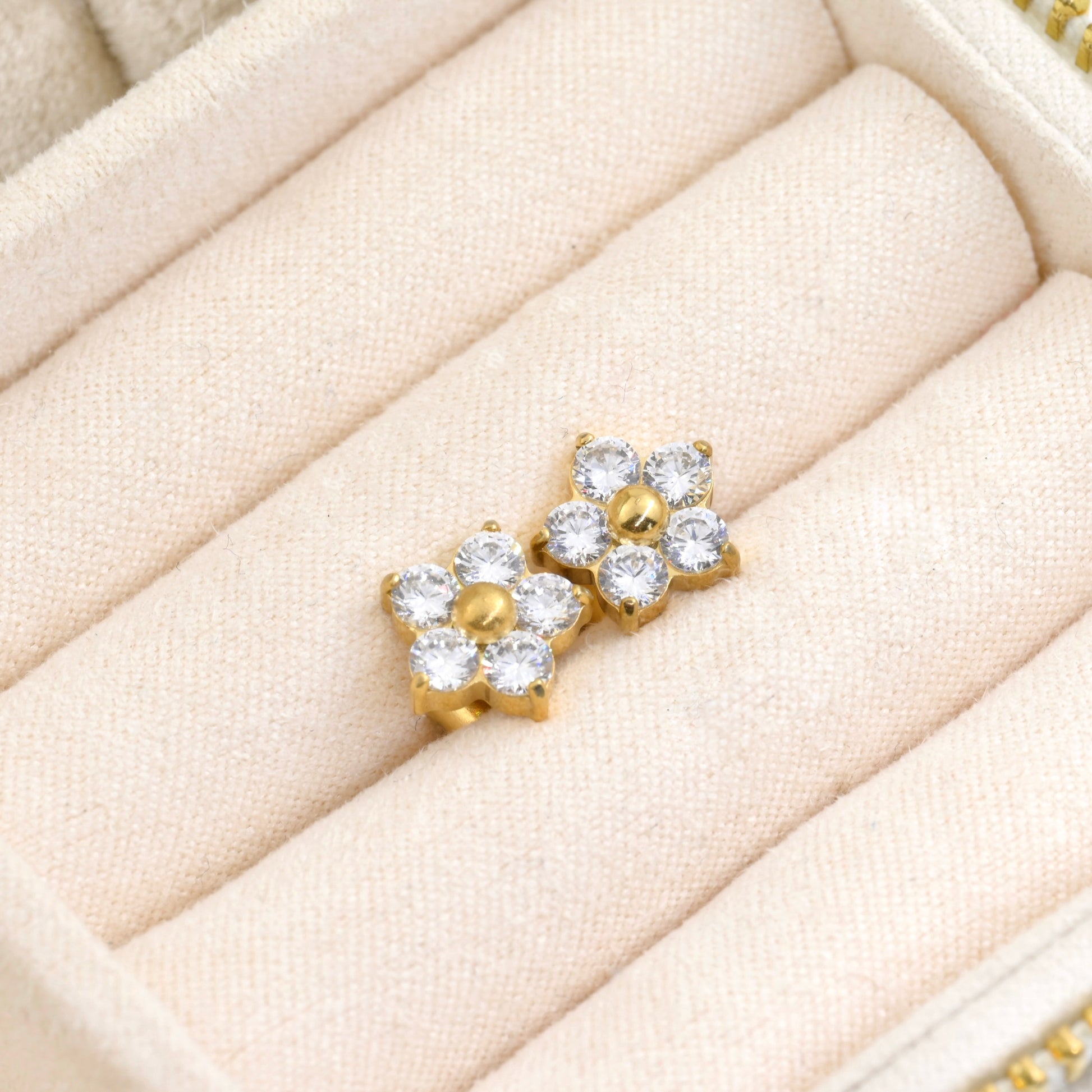 Small gold flower earrings with diamonds in a beige jewelry display tray