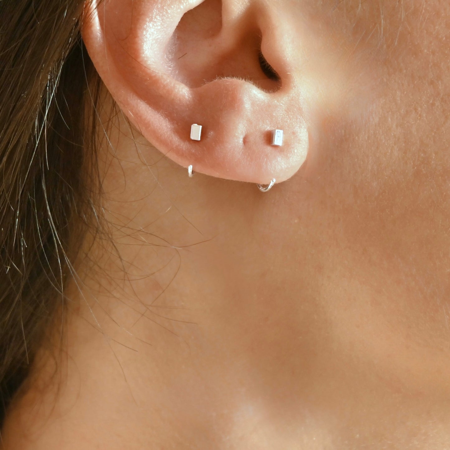 Close-up of a person's ear showing one small and one slightly bigger rectangular block  hoop earrings.