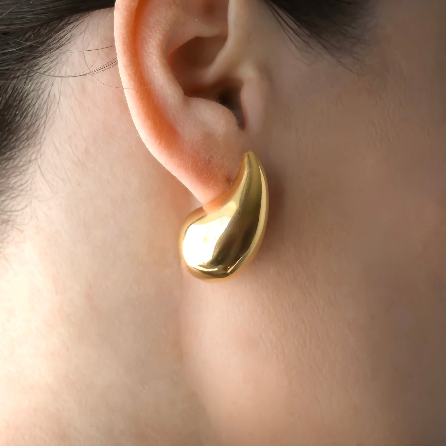 Gold bottega earring worn on an ear with a blurred background