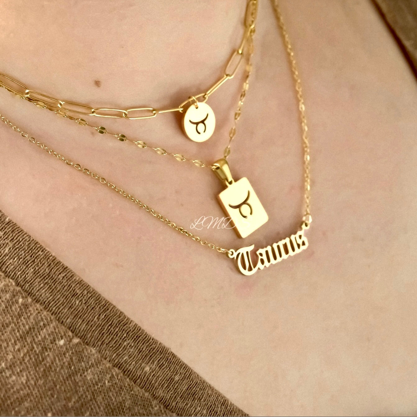 Gold necklaces with zodiac pendants  layered on a person's neck