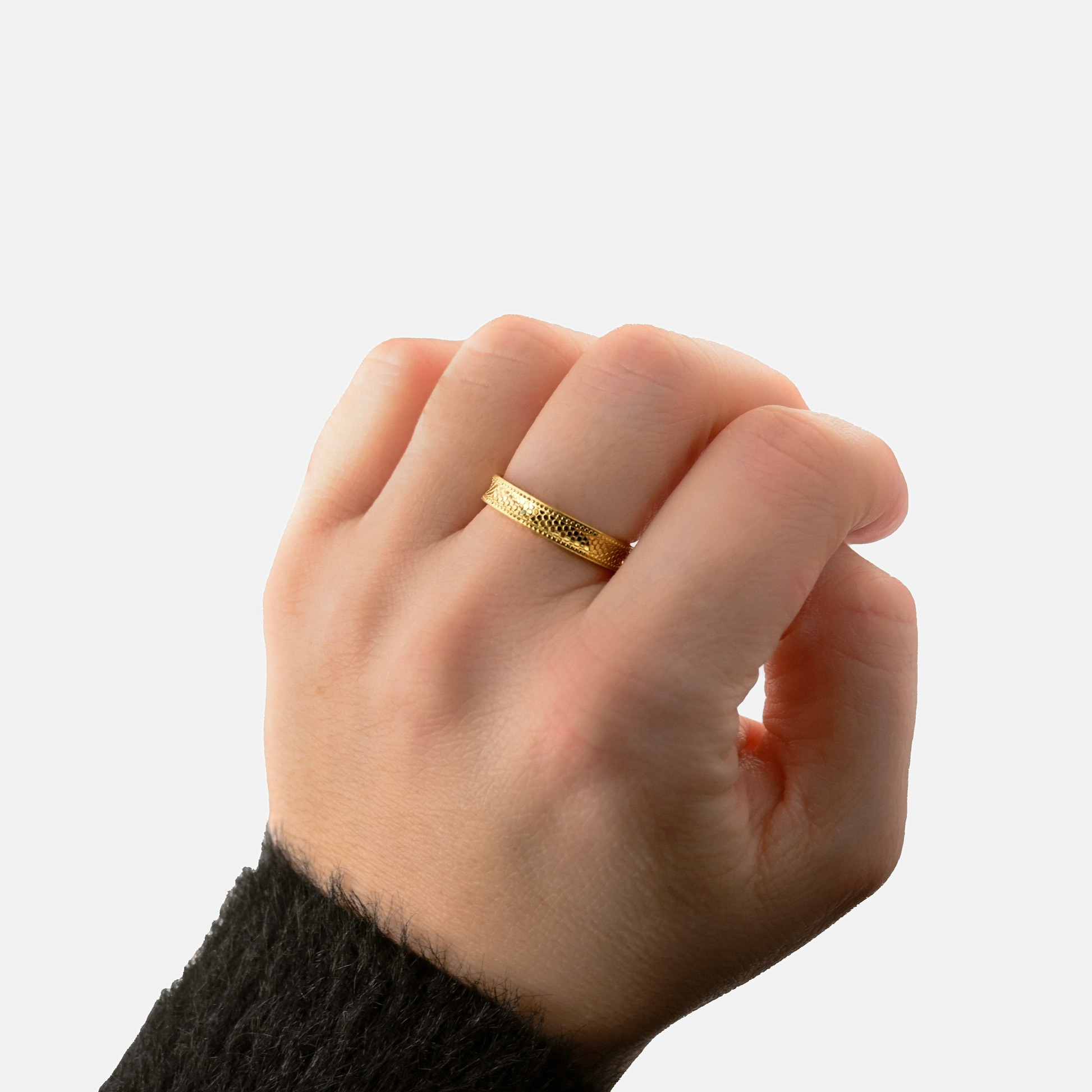A close-up of a person's hand wearing a textured yellow gold band ring, set against a clean light gray background.