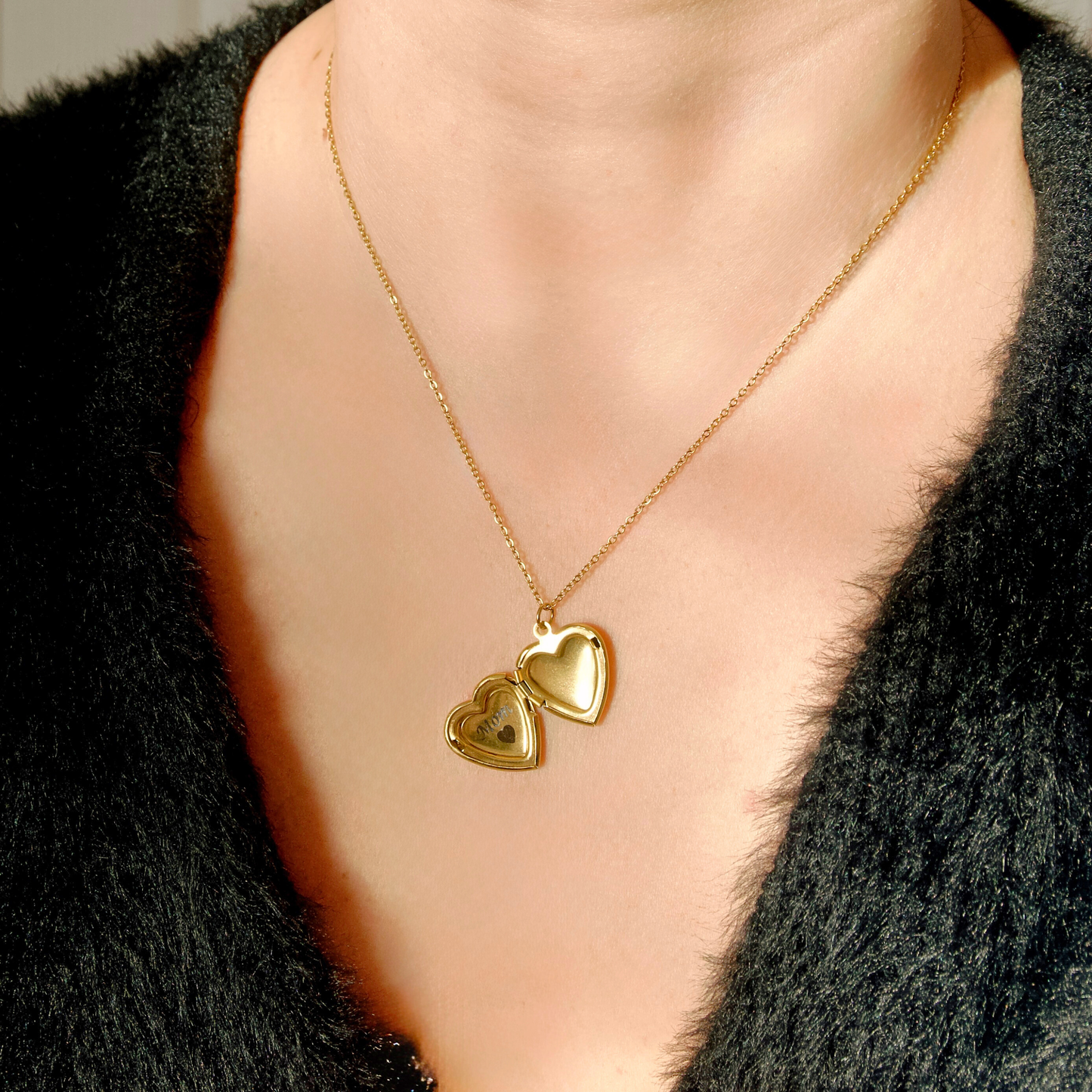 Gold heart open locket necklace on a person wearing a black garment.