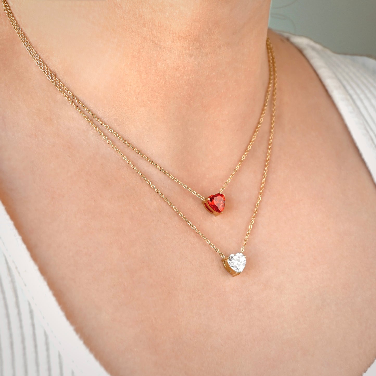 Two gold necklaces with garnet and diamond heart solitaires on a person's neck.