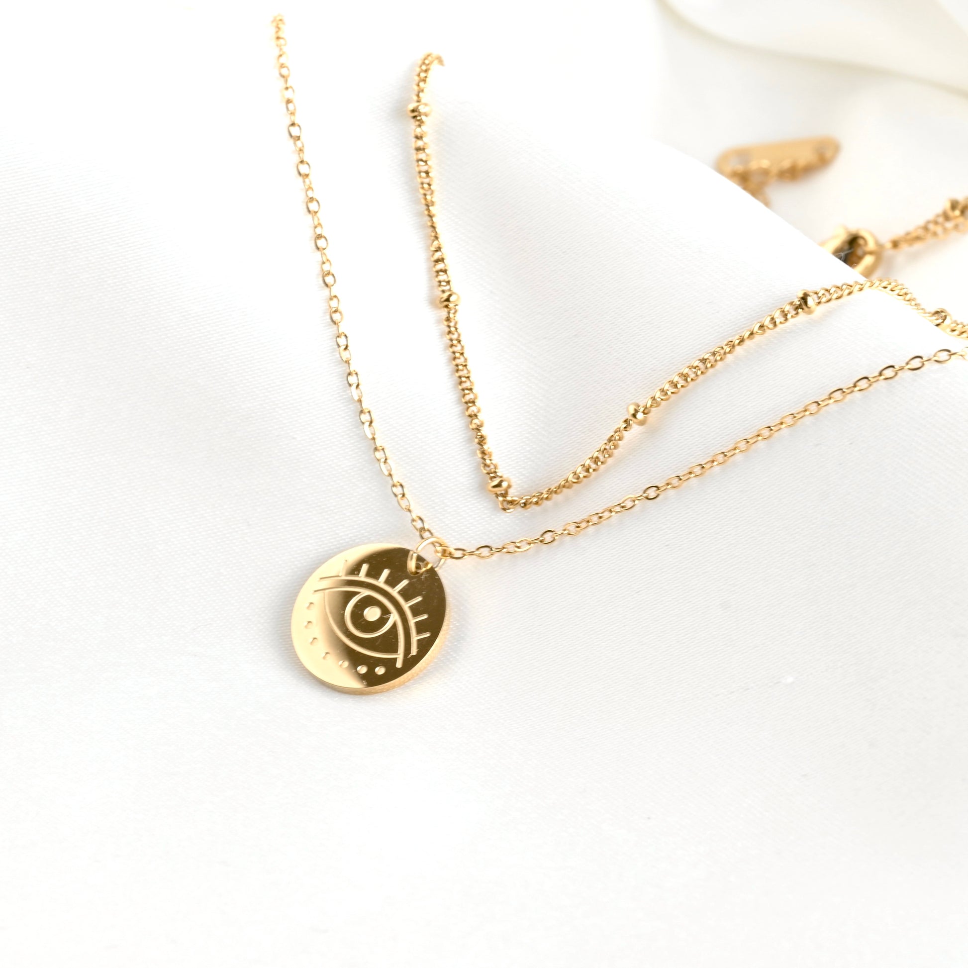 Gold necklace with a circular pendant featuring an eye design on a white background