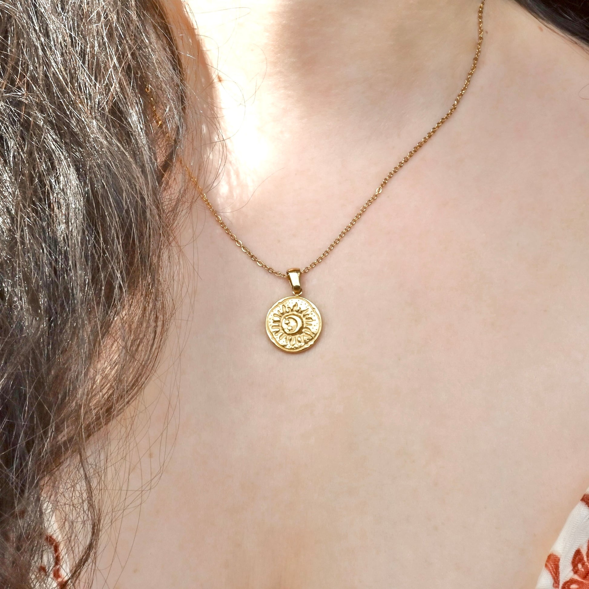 Gold necklace with a circular pendant with an embossed sun and moon worn by a person