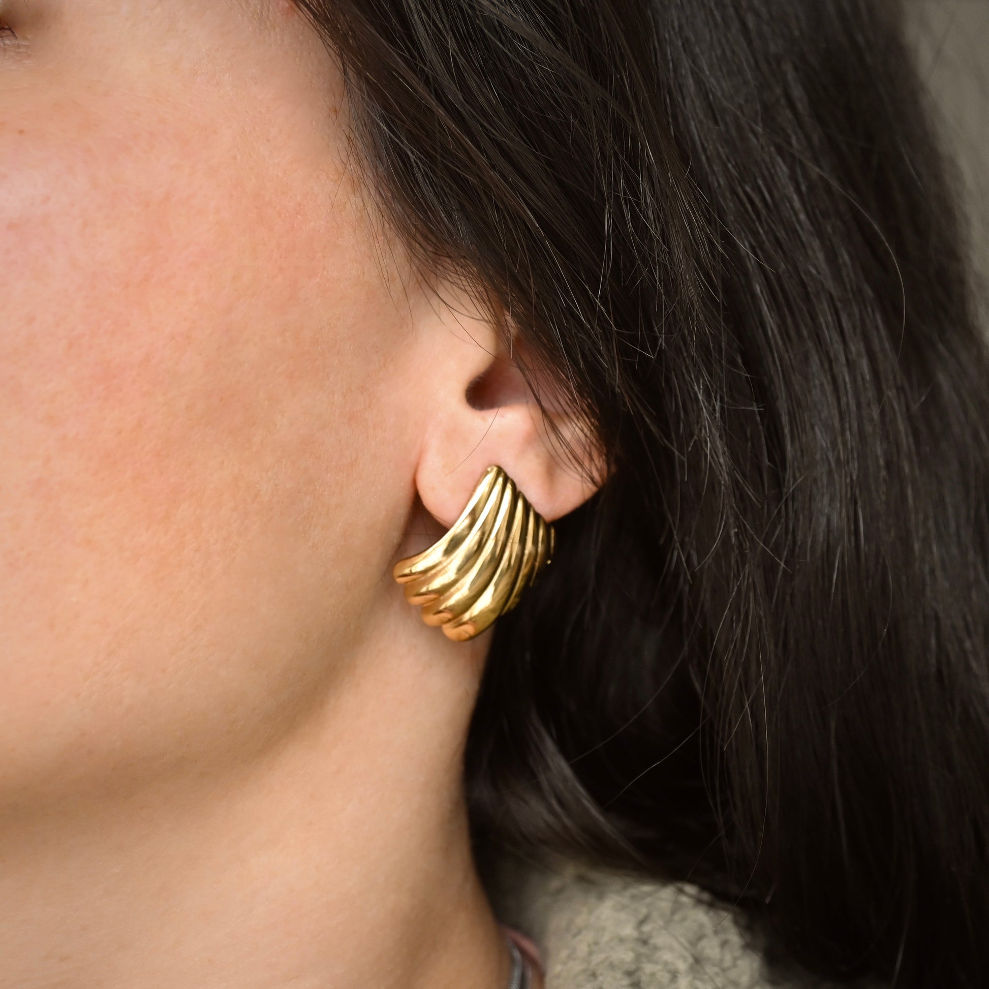 Gold geometric hoop earrings with a ribbed design worn by a person with dark hair.