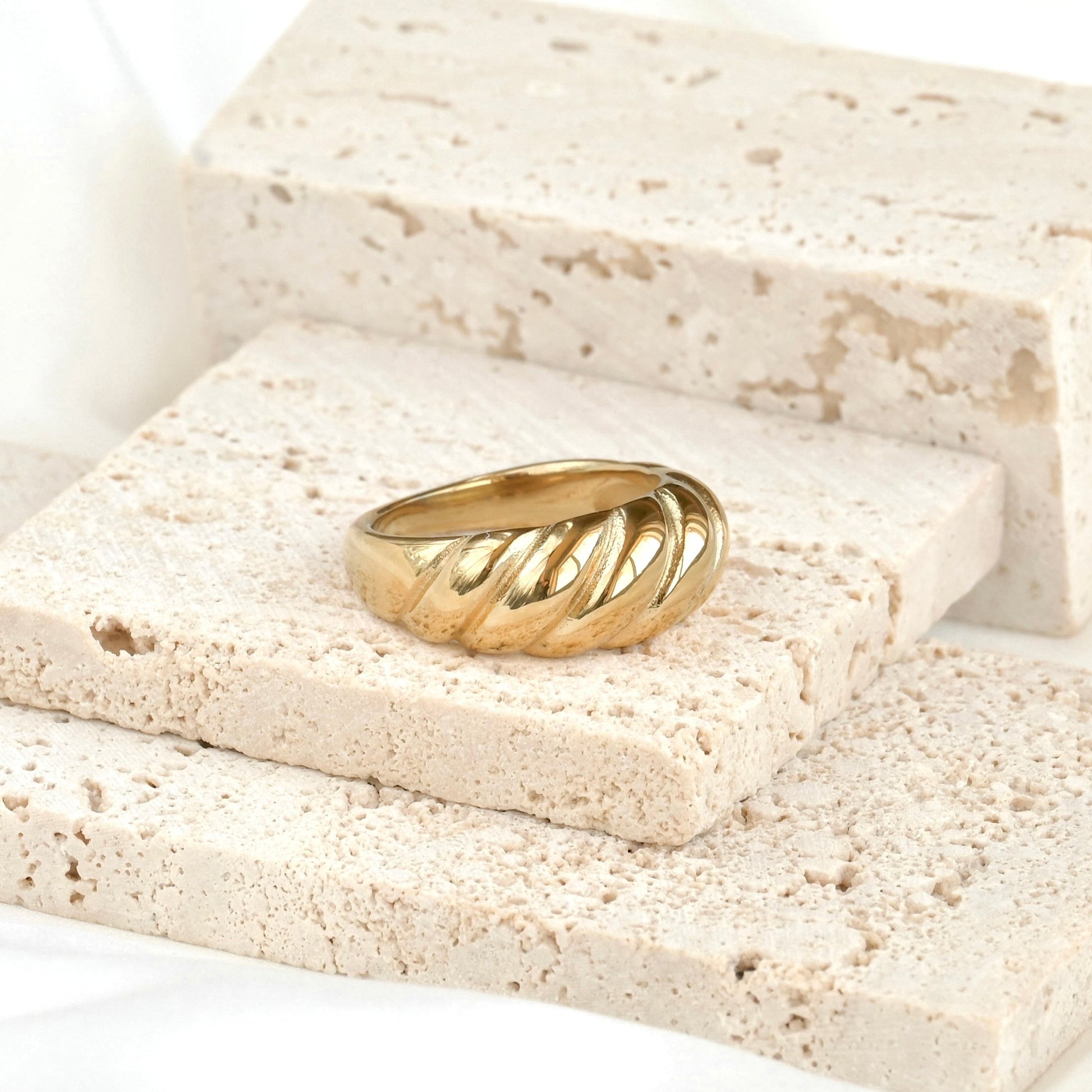 Chunky gold croissant ring on a stone surface with a white background
