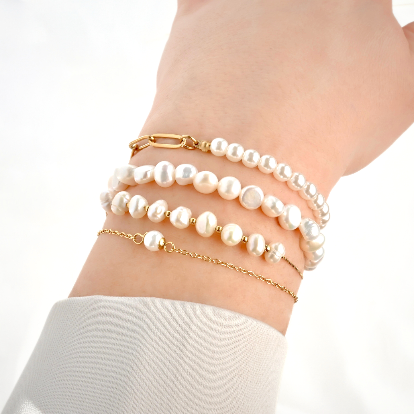 Pearl and gold bracelet set on a wrist against a white background