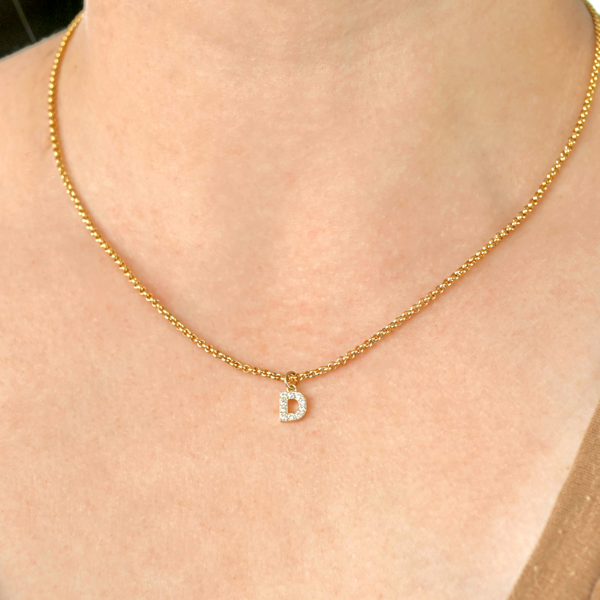 Gold rolo necklace with a pave CZ  'D' pendant on a person's neck