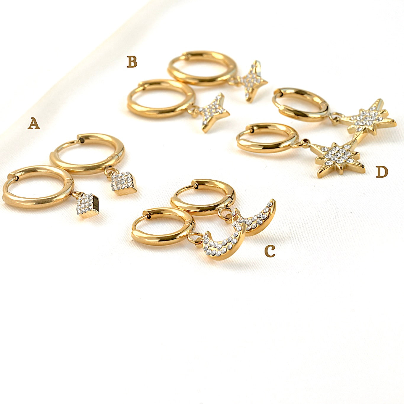 Set of four gold charm hoop earrings with crystal celestial charms on a white background