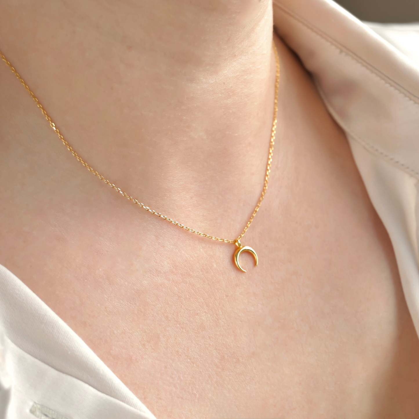 Gold necklace with a small  horn pendant on a person wearing a white shirt.