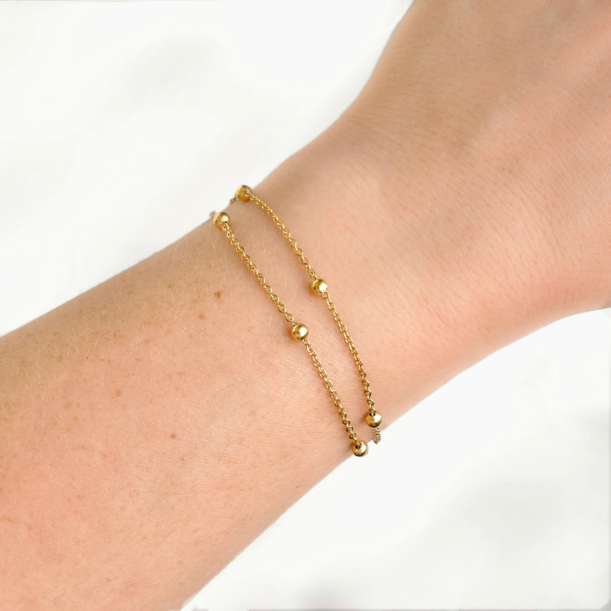 A delicate gold chain bracelet with small bead accents worn on a person's wrist, shown against a clean white background.