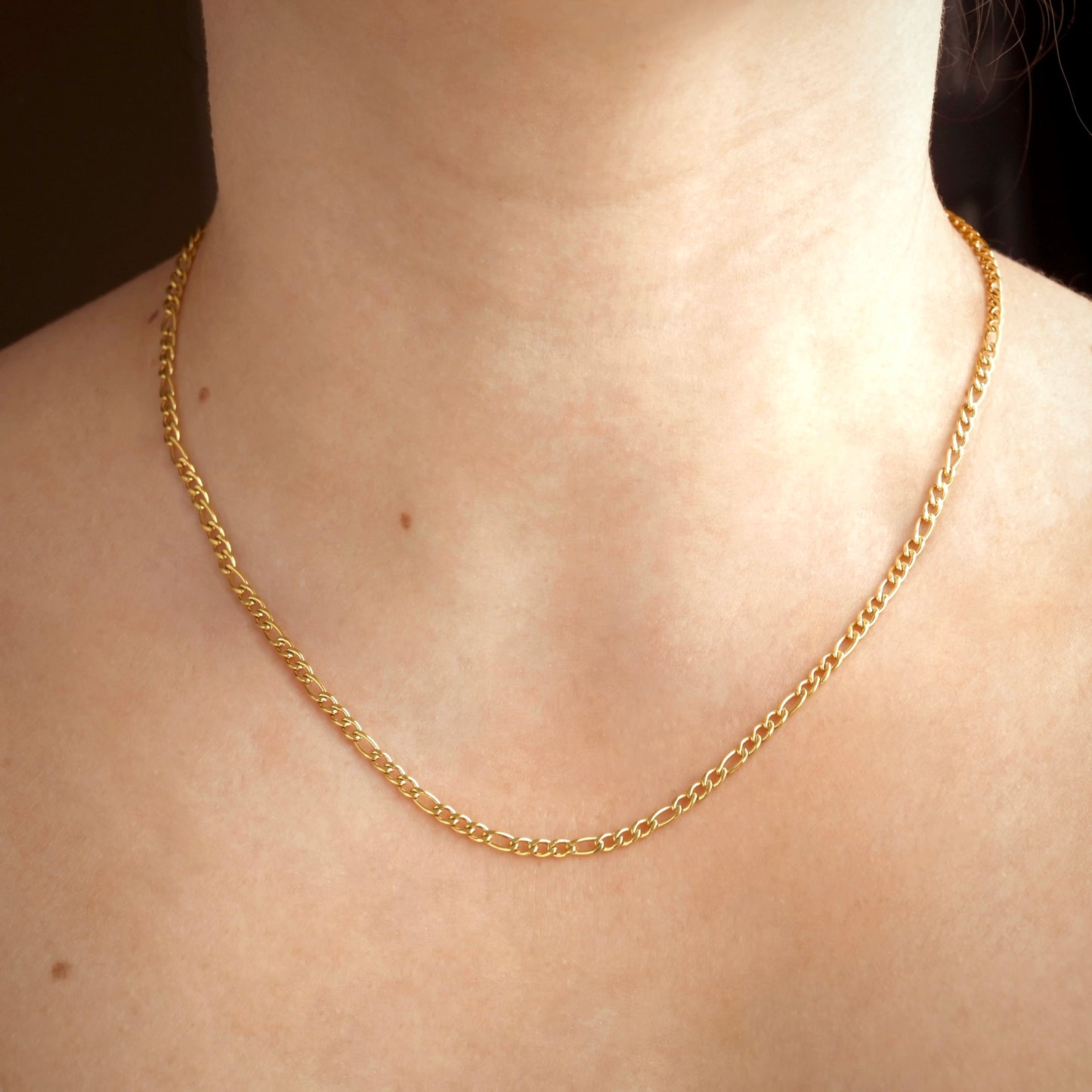 Front view of gold figaro necklace on a person's neck against 