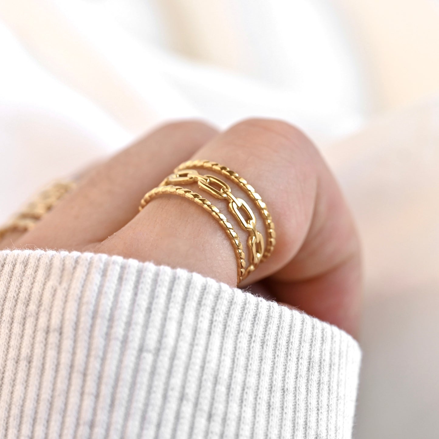 Layered gold curb chain ring on a finger with a blurred background