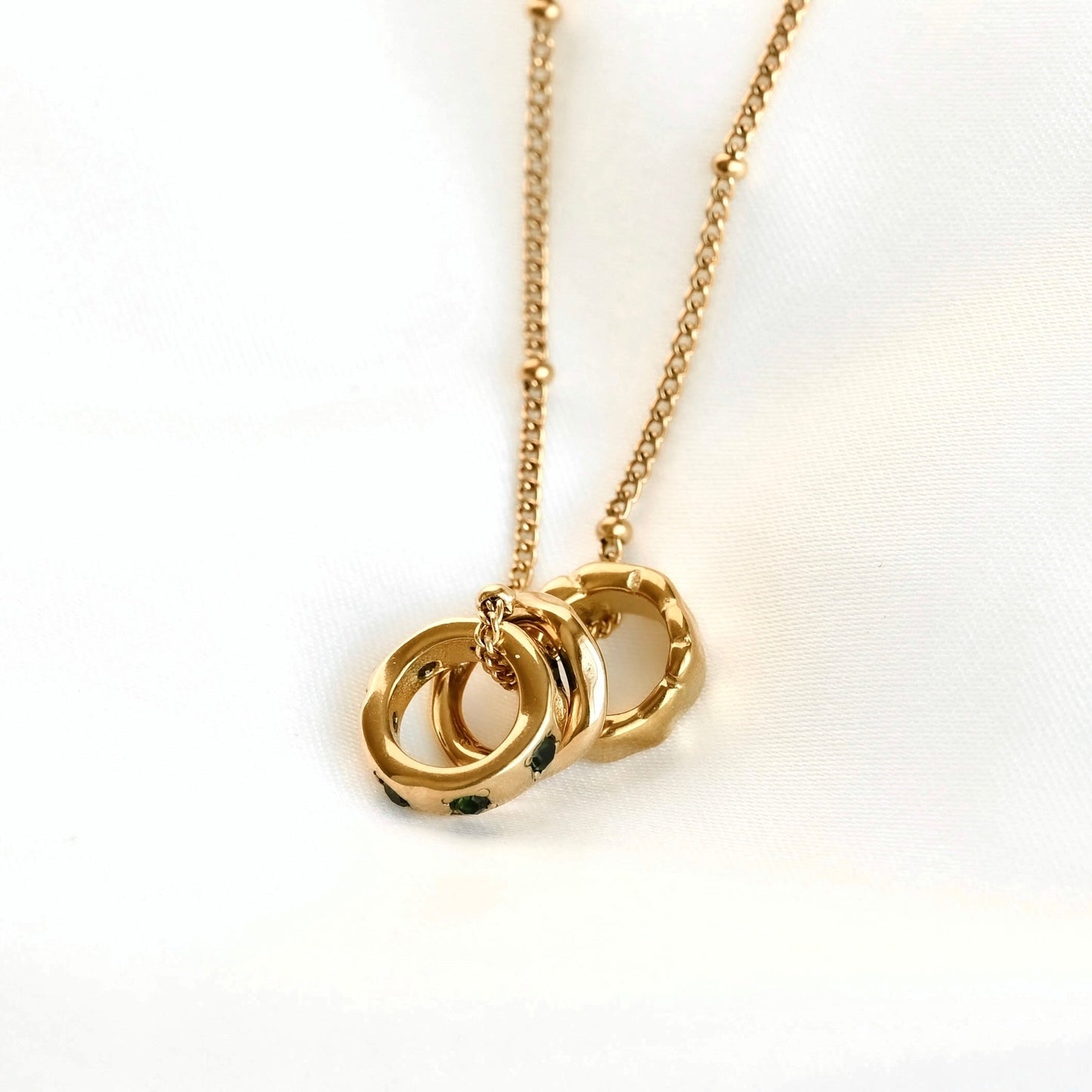 A gold necklace with a delicate chain and a pendant consisting of three rings set against a plain white background.