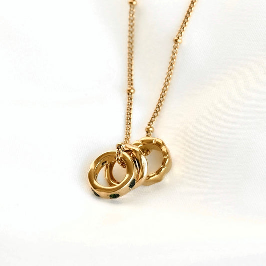 A gold necklace with a delicate chain and a pendant consisting of three rings set against a plain white background.