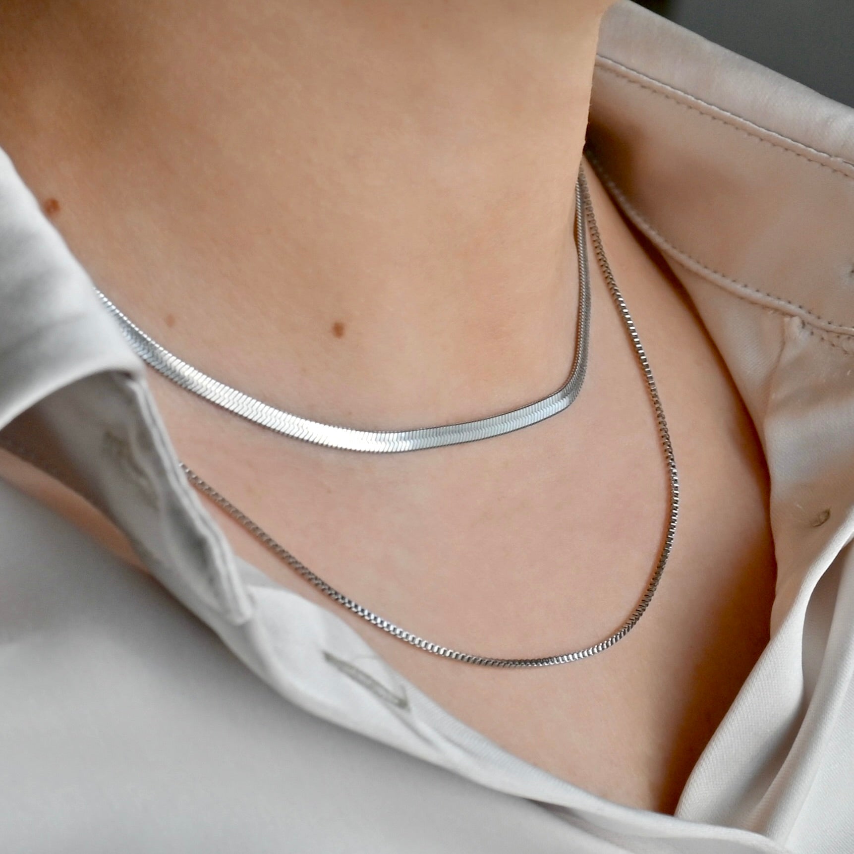 Silver 20-inch box chain layered with a 16" herringbone chain on a person wearing a white shirt