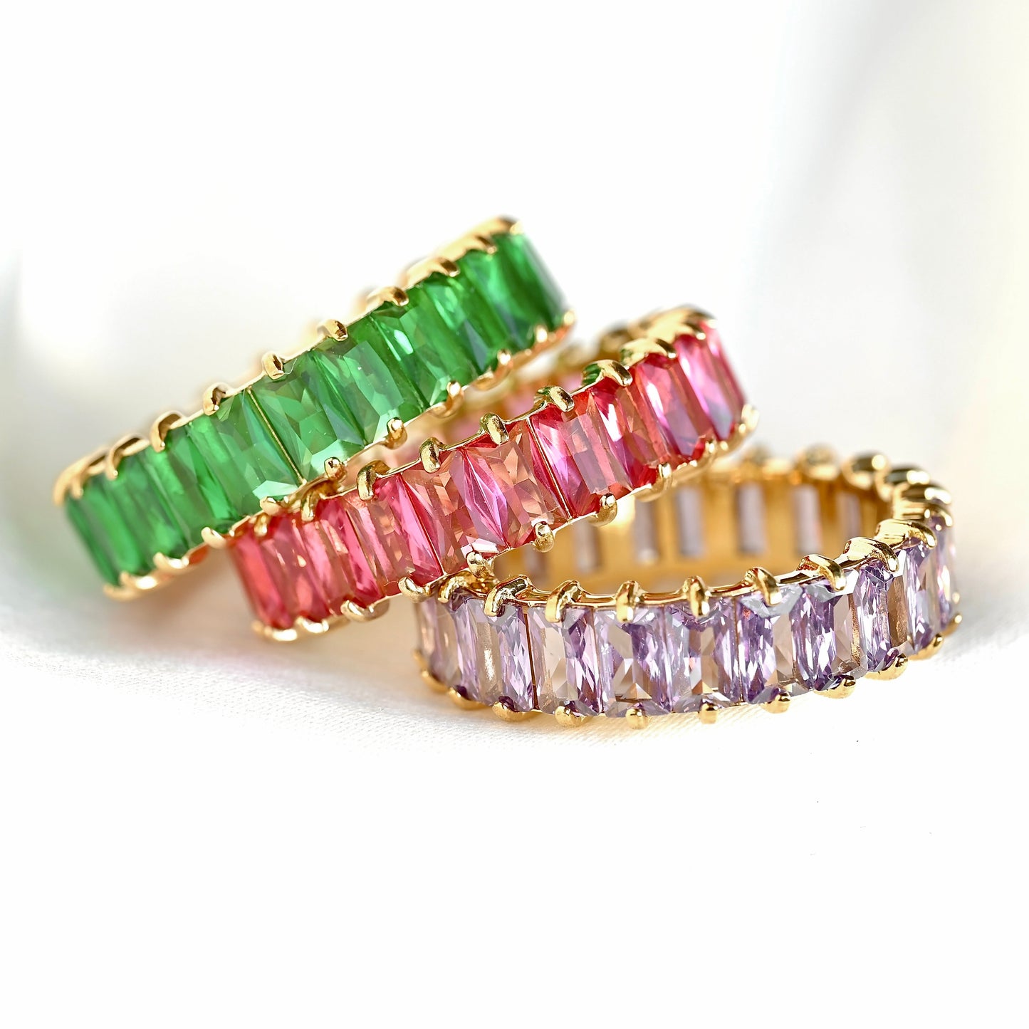 Three gold rings with green, pink, and purple gemstones on a white background