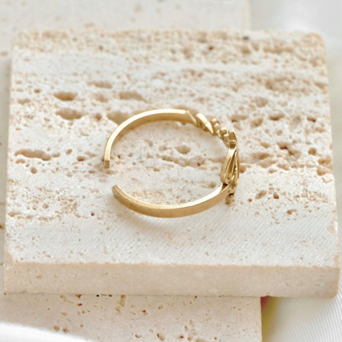 A delicate gold open ring with a smooth open band, resting on a textured beige stone tile.