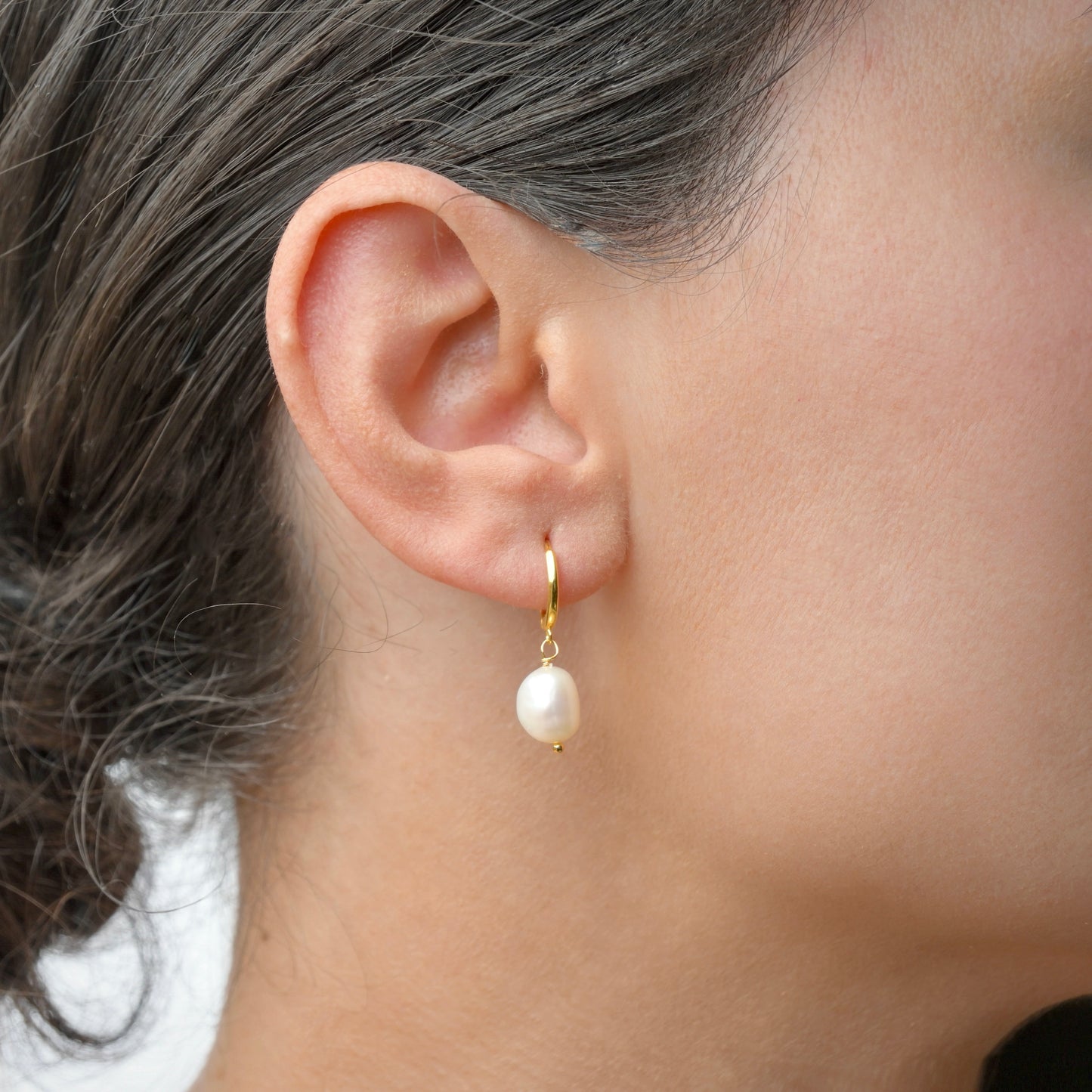 Gold Pearl earring worn by a person with a neutral background