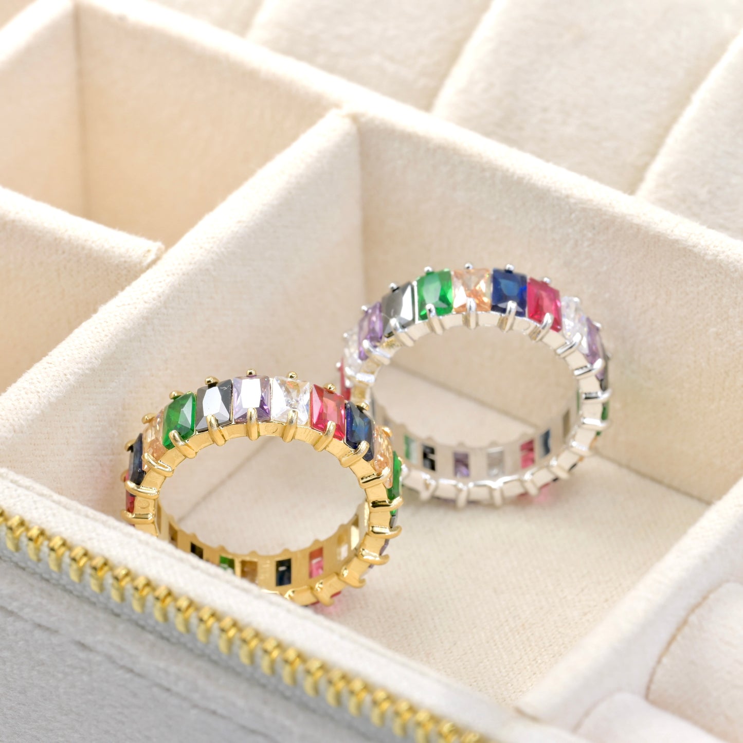 One gold and one silver ring with rainbow colored gemstones in a jewelry box.