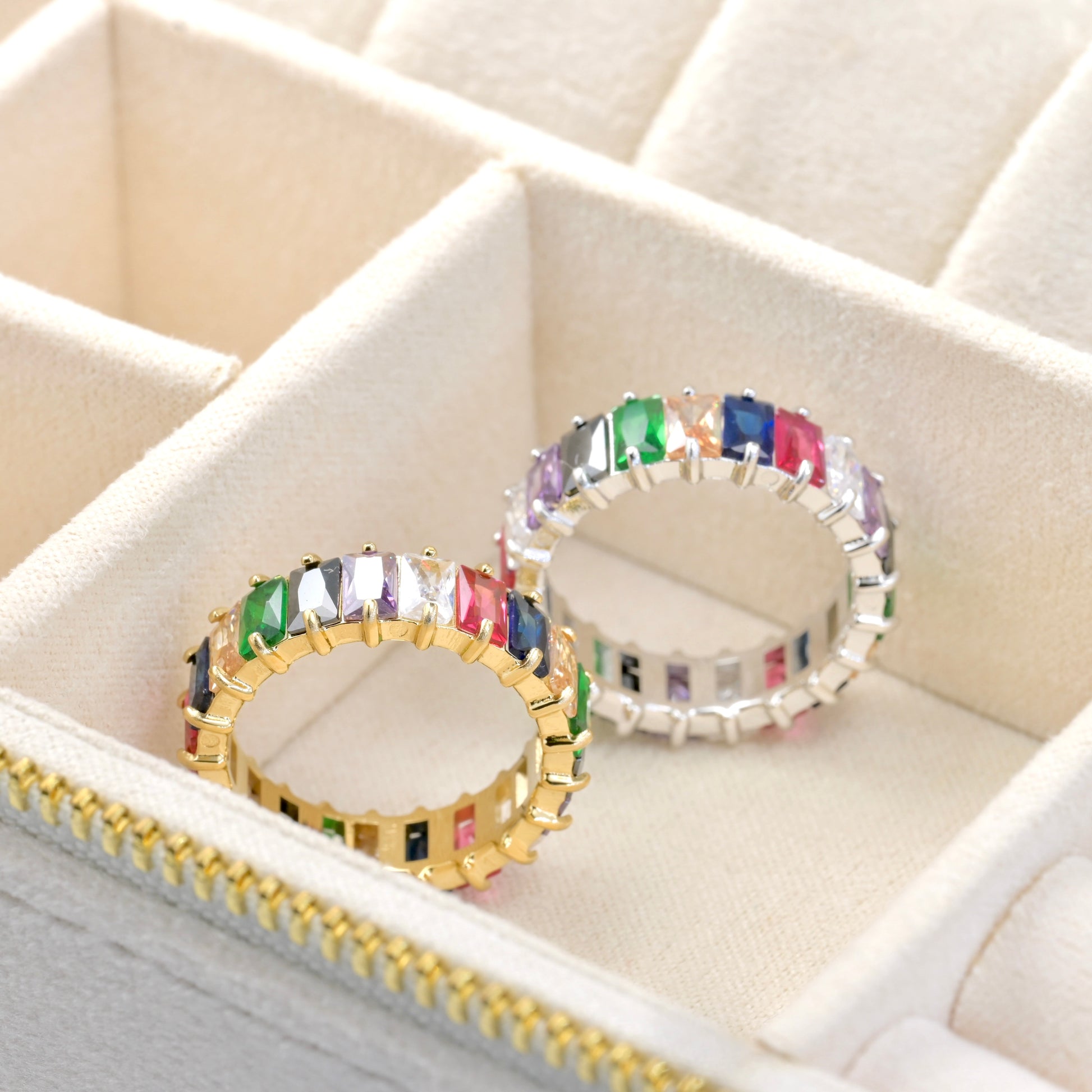 One gold and one silver ring with rainbow colored gemstones in a jewelry box.