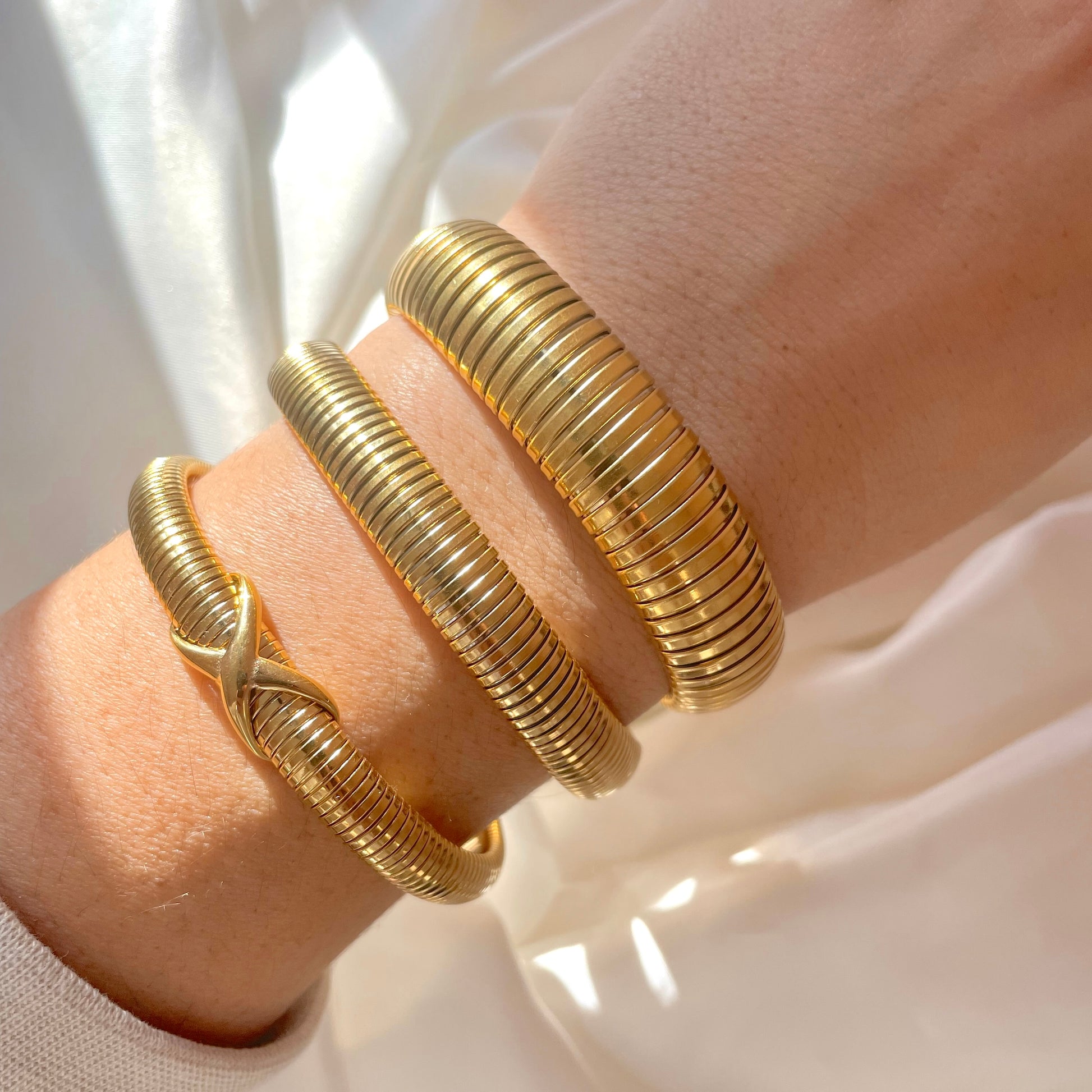 Gold tubogas bracelets on a wrist with a soft white background