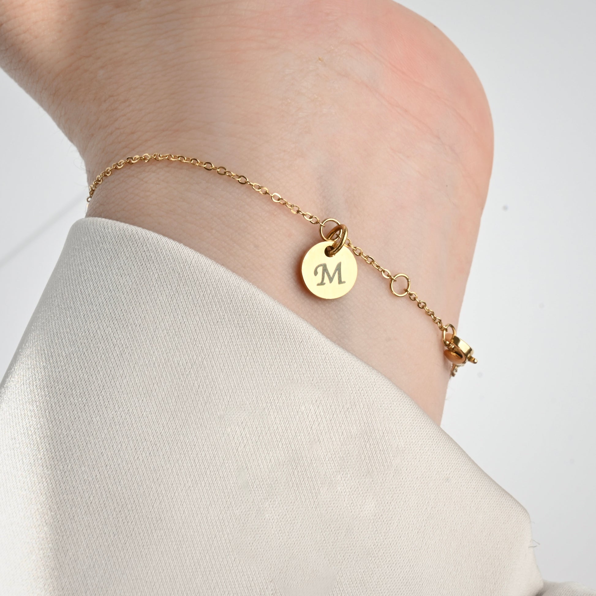 Gold circke bracelet with a small disc charm with letter 'M' at the clasp area