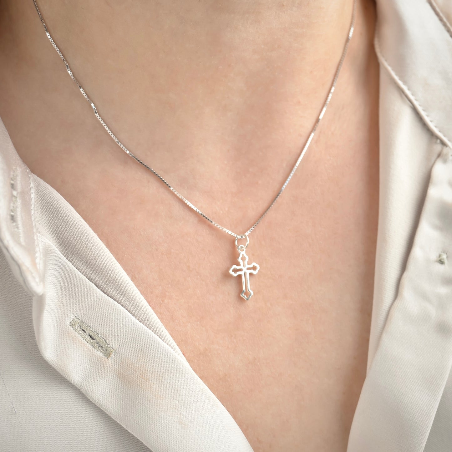 Silver cross necklace on a box chain on person wearing a white shirt