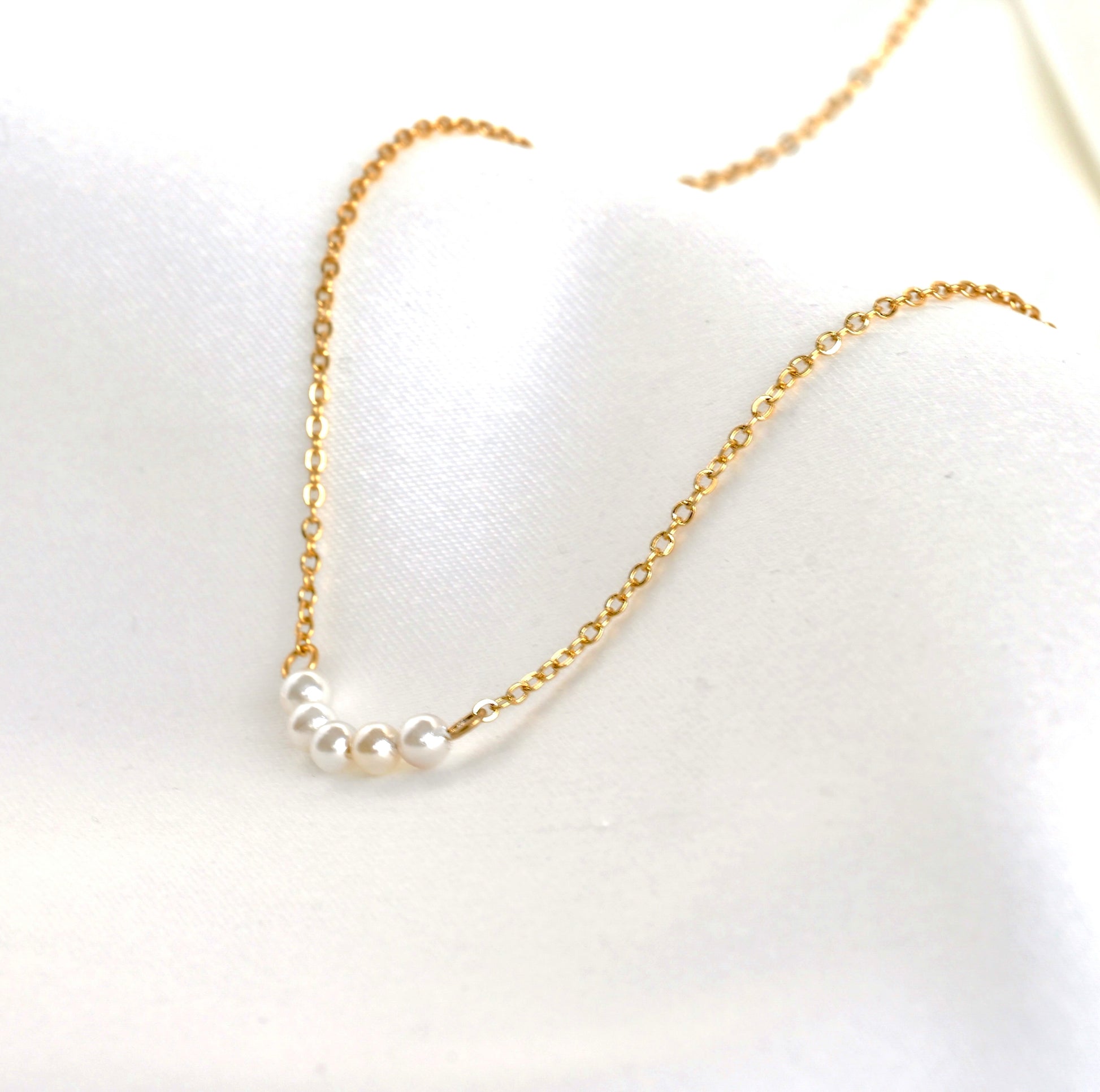 Angled view of gold pearl bar necklace with  tiny pearls on a white background