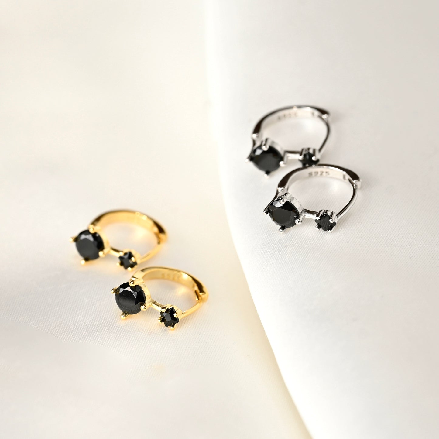 Pair of gold and silver earrings with black gemstones on a light background