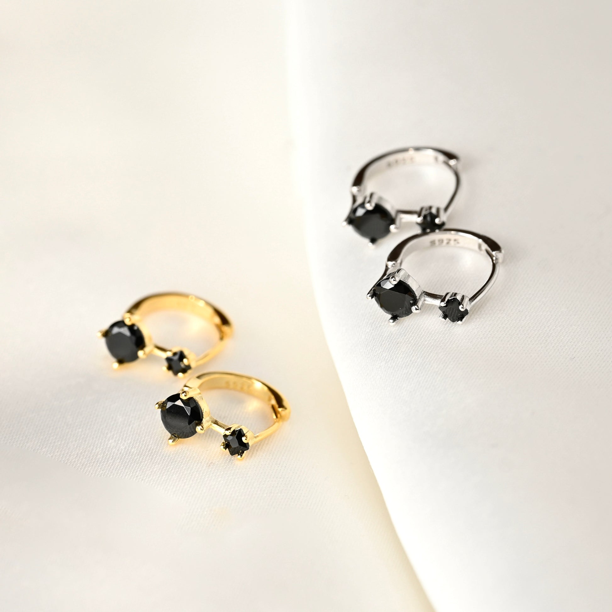 Pair of gold and silver earrings with black gemstones on a light background