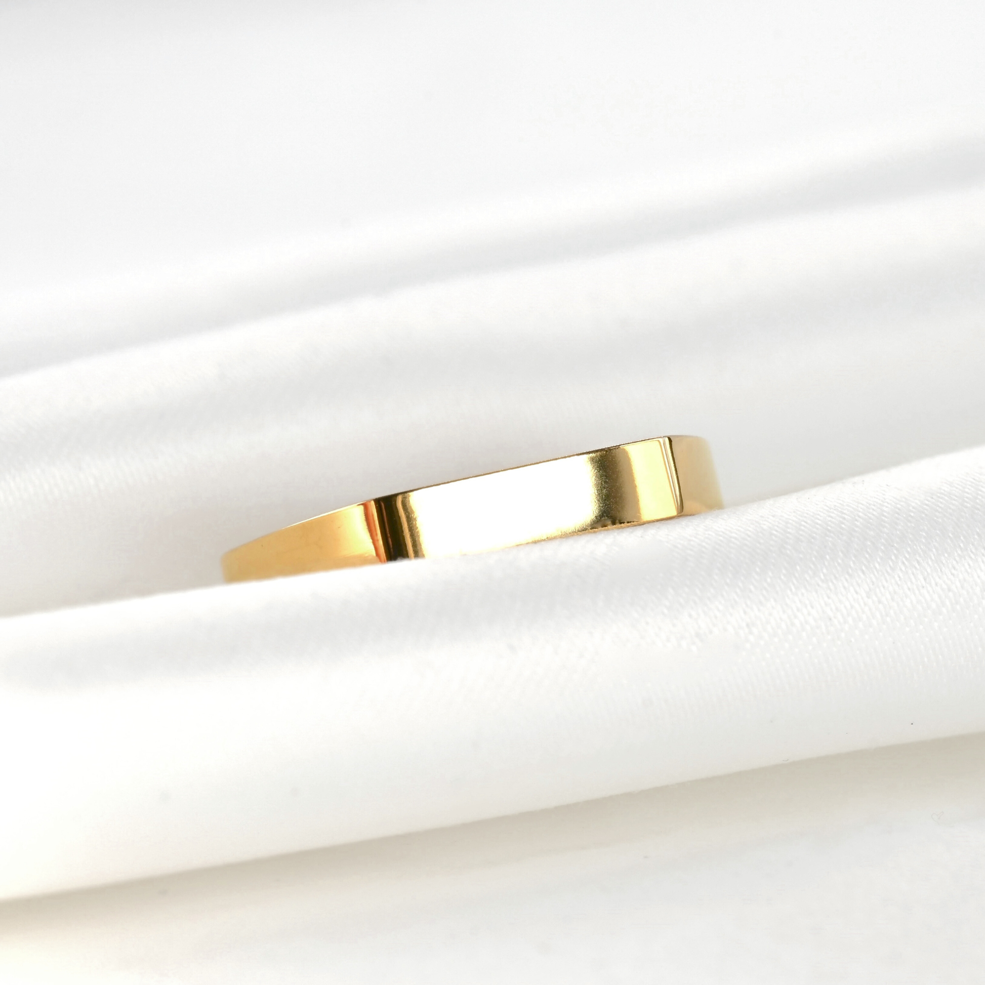 Gold bar ring reflecting light on a white fabric background