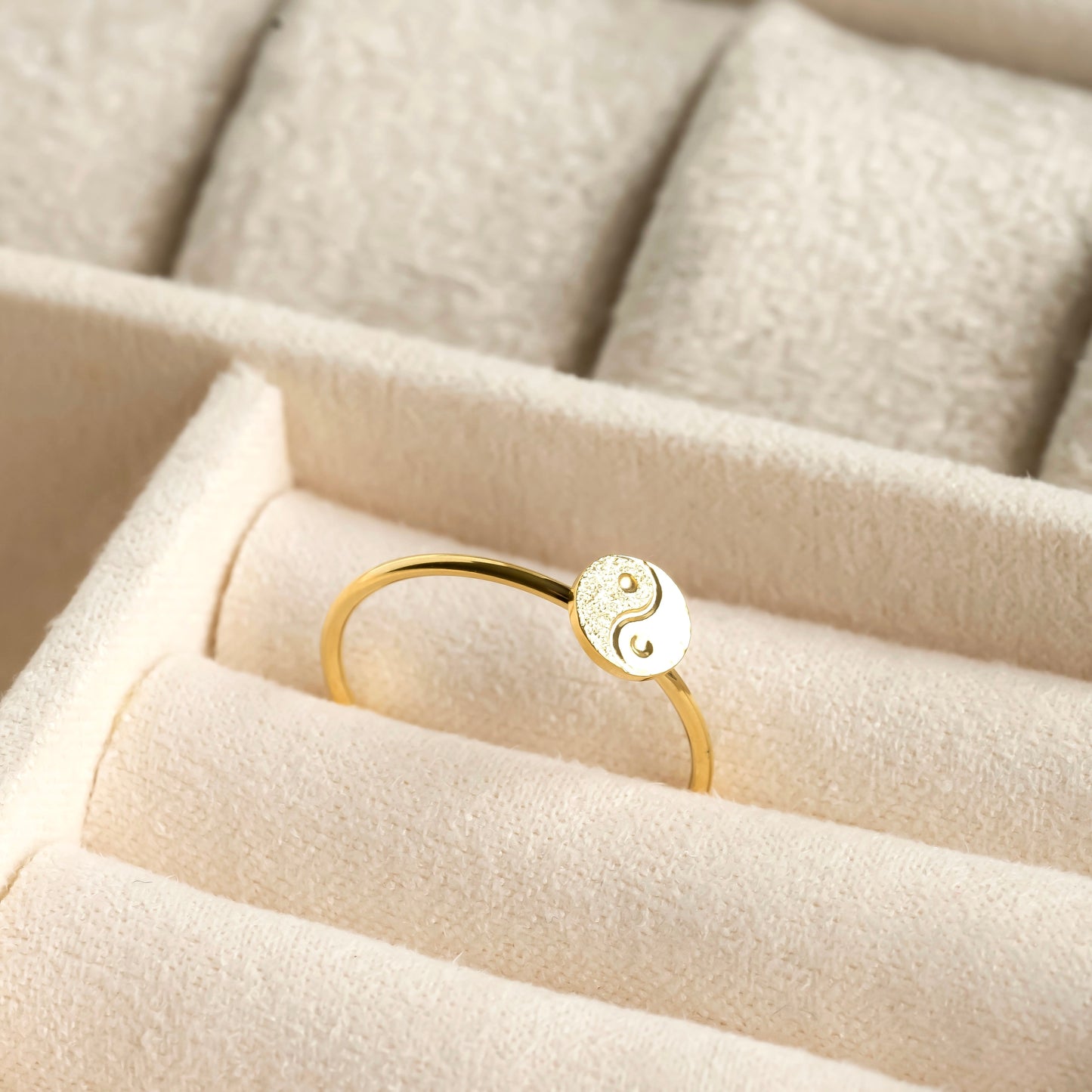 Gold duality ring with a yin yang symbol on a beige cushion