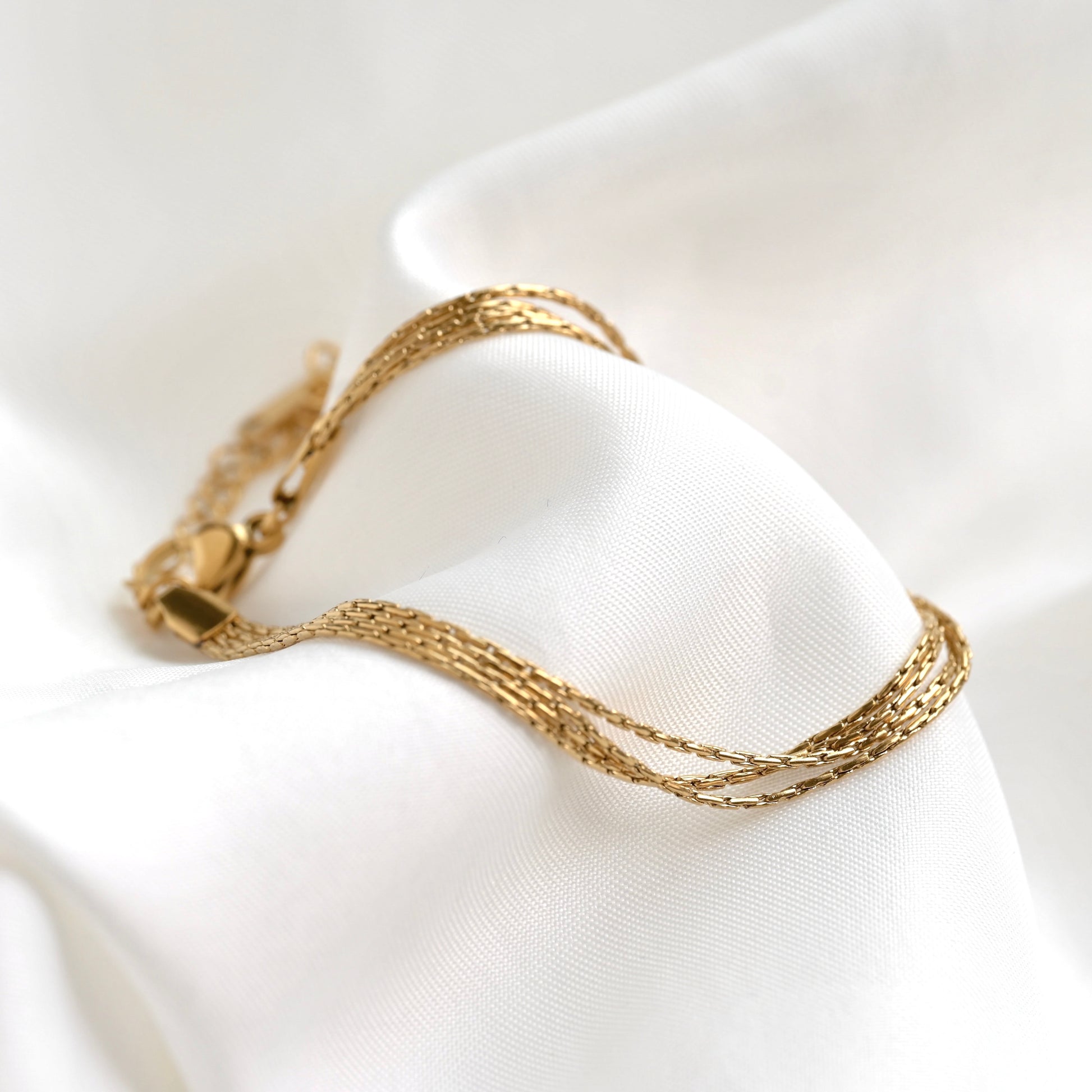 A delicate gold chain bracelet draped over soft white satin fabric.