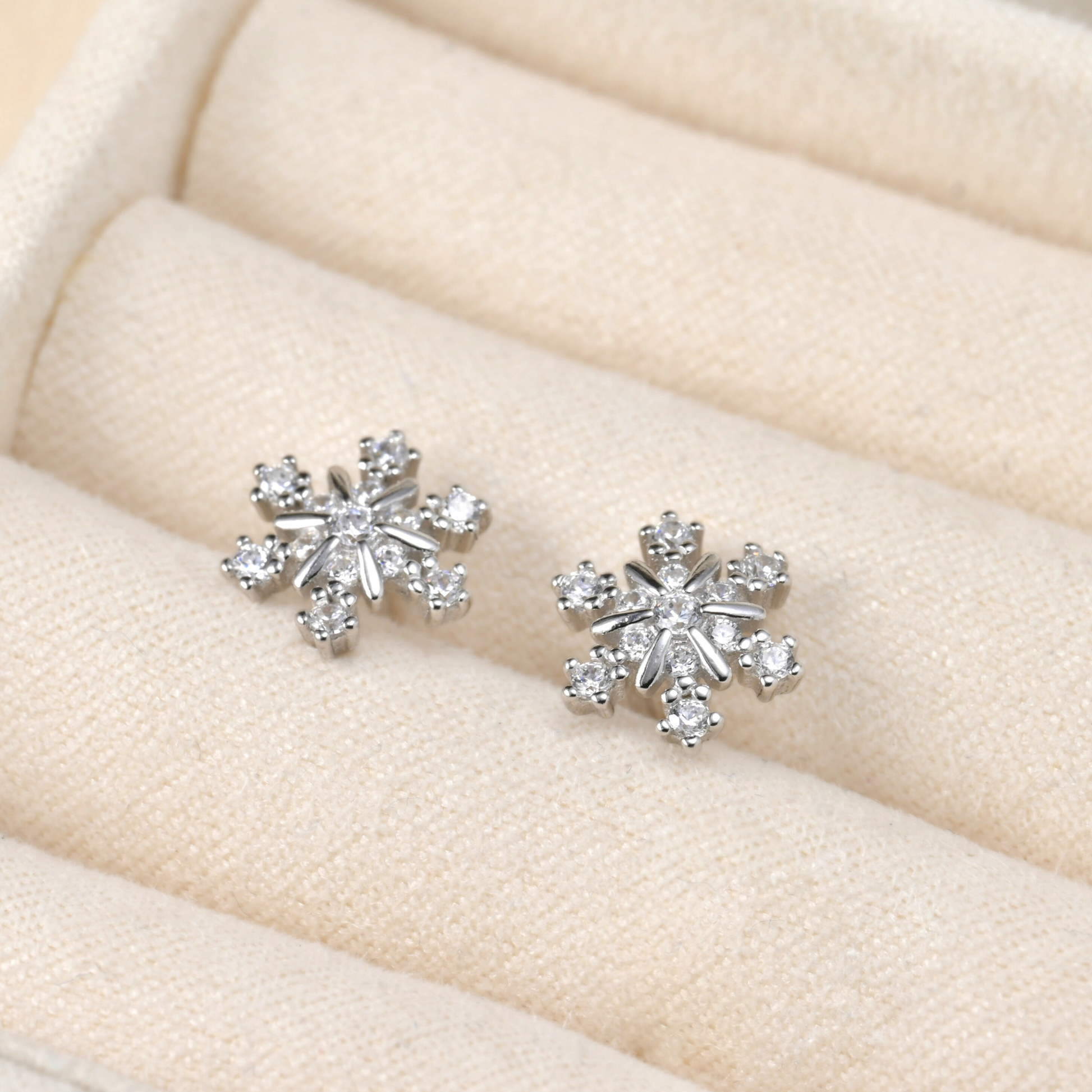 Silver snowflake earrings on a beige cushion