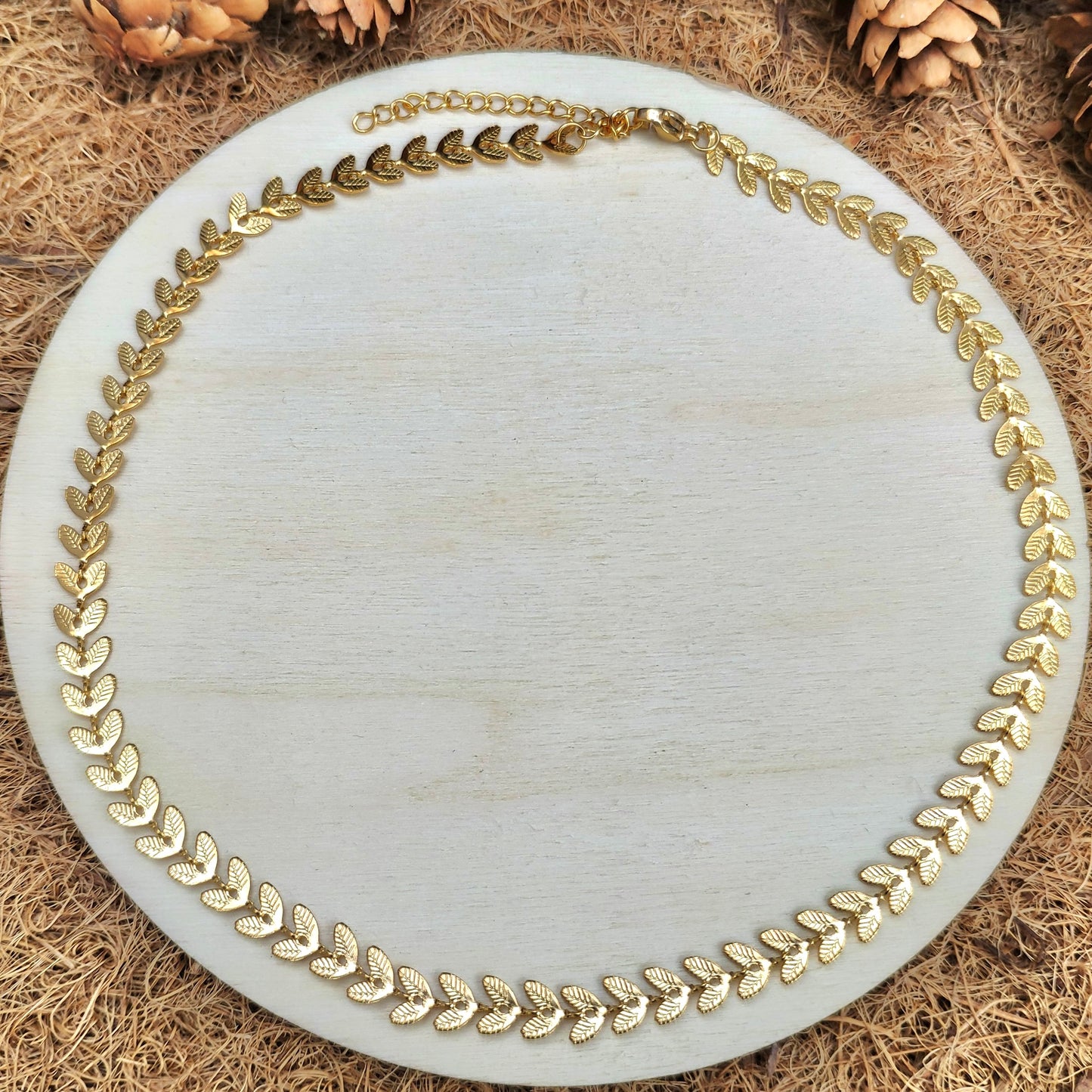 Wide angled top view of gold lchevron chain necklace on a round white plate with a natural wood background