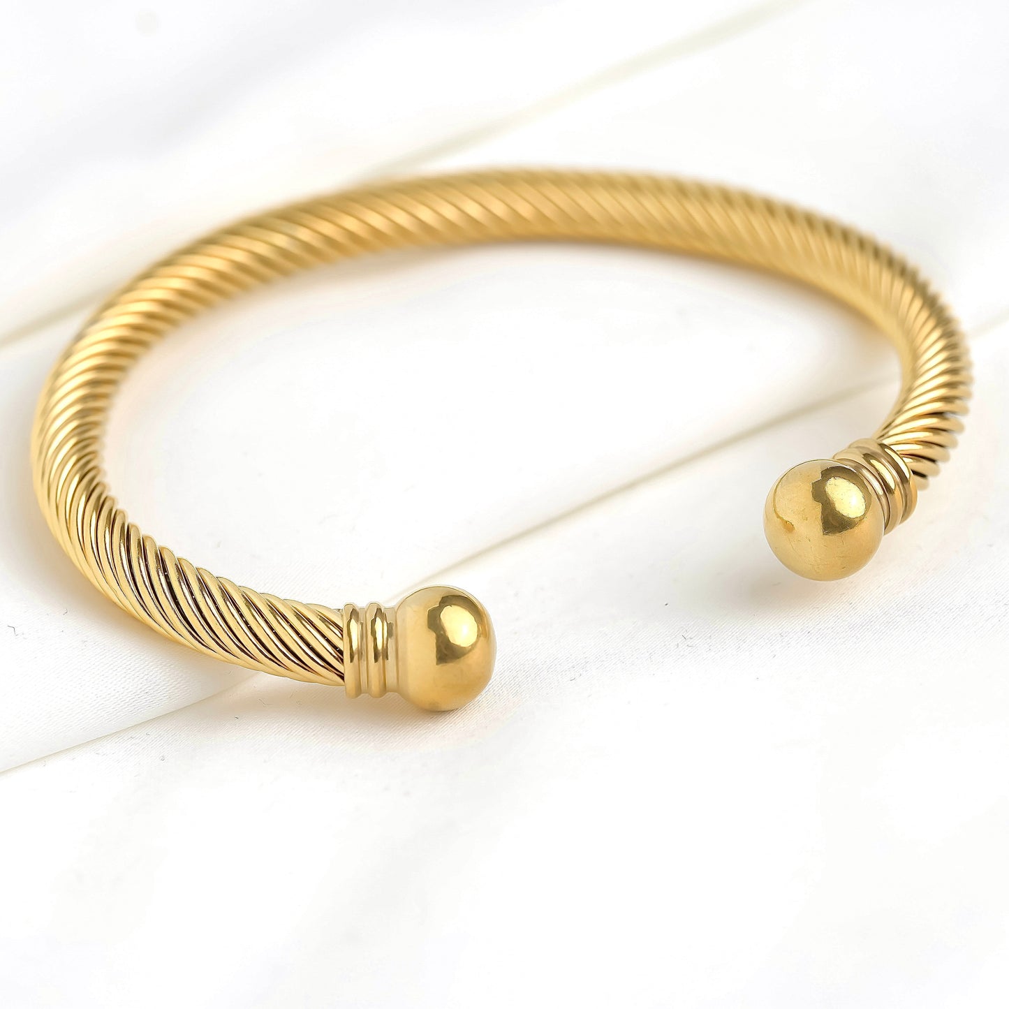 Gold cable flex bracelet with ball ends on a white background