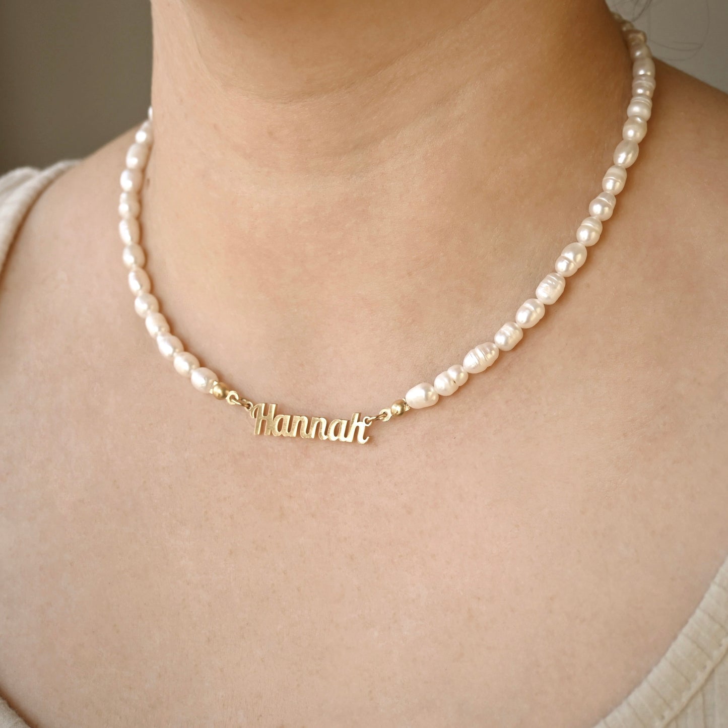 Pearl necklace with a gold name pendant on a person wearing a beige top.