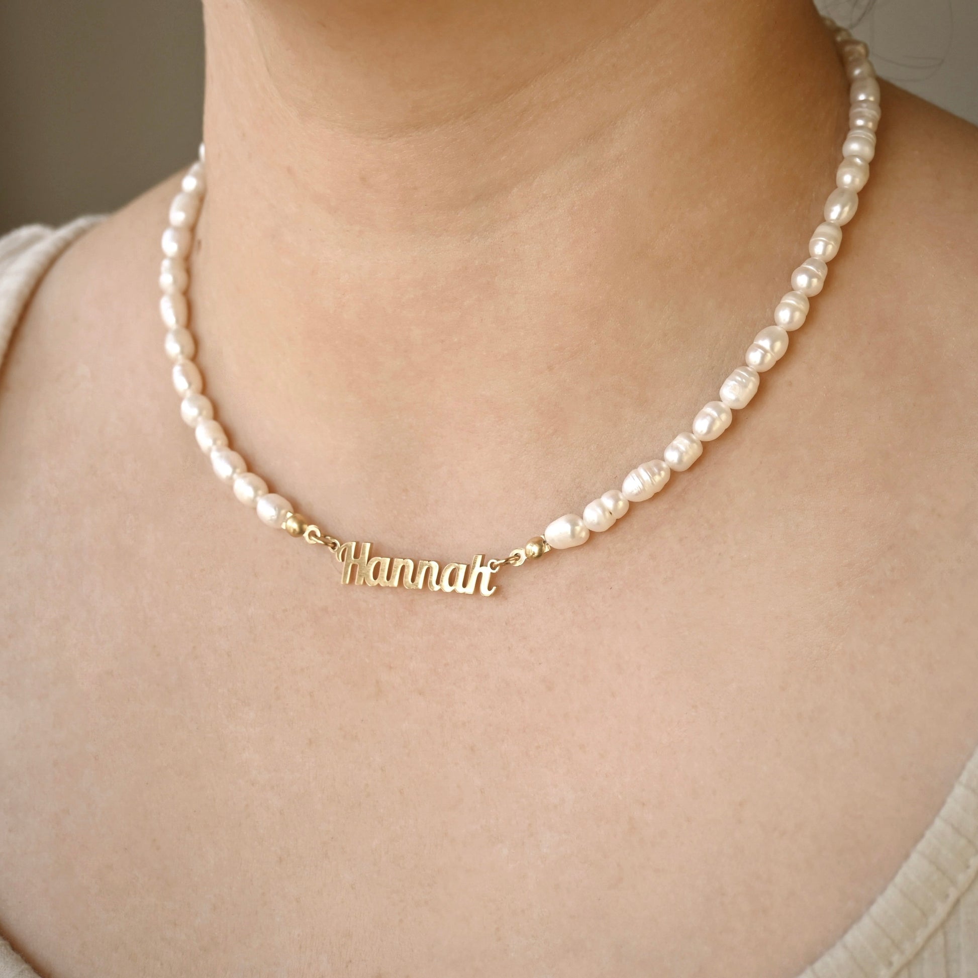 Pearl necklace with a gold name pendant on a person wearing a beige top.