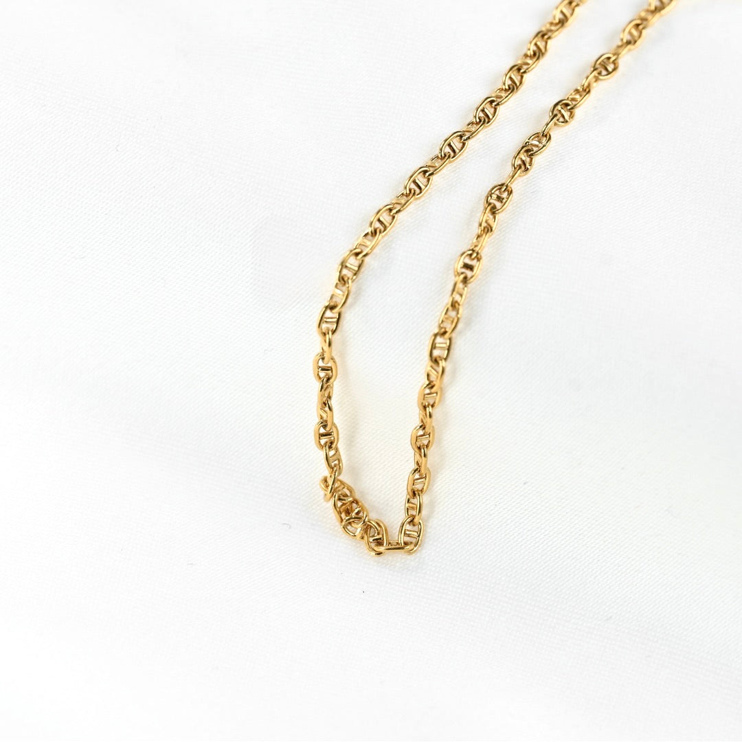 A close-up of a gold chain necklace on a white textured fabric background.