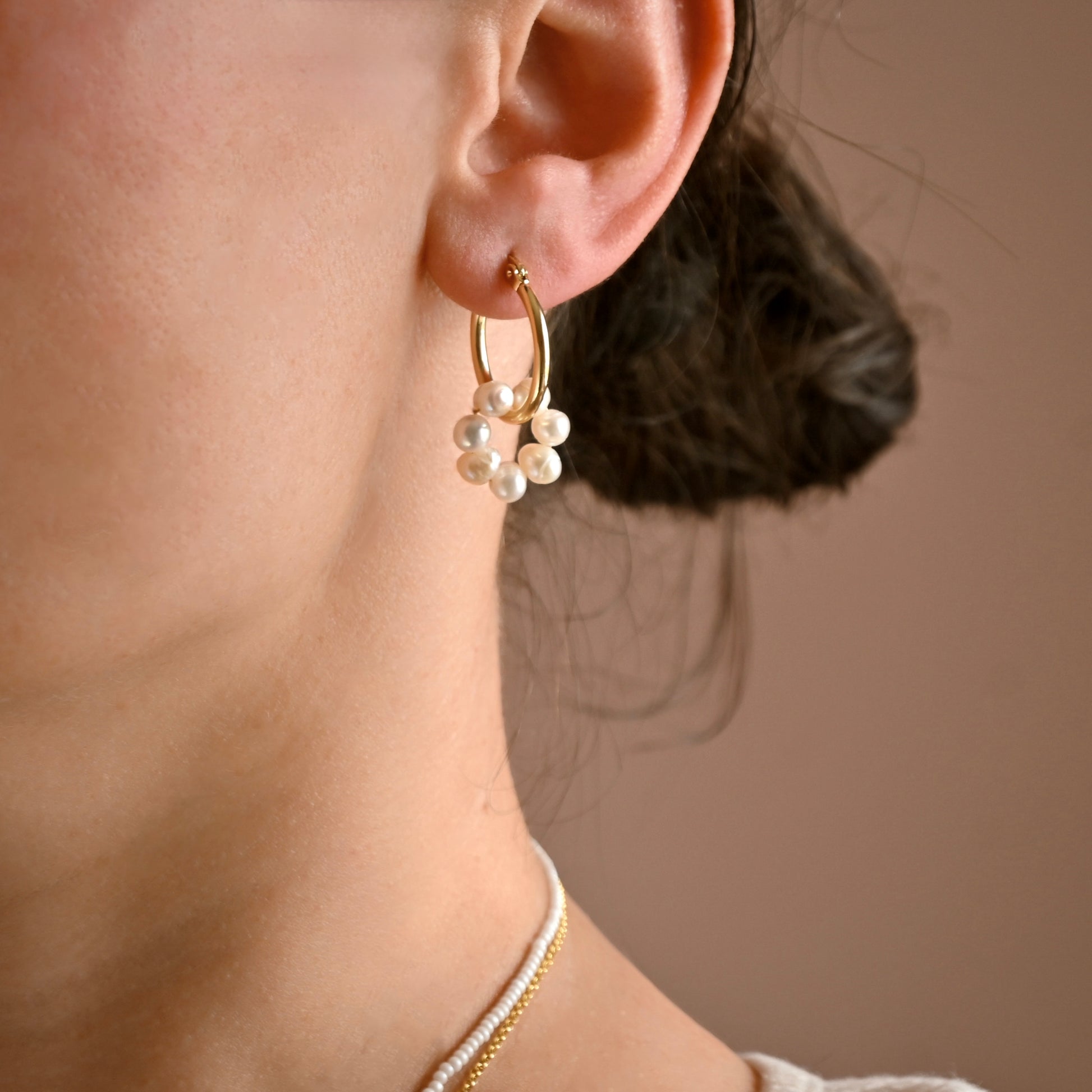 Close-up of an ear wearing a gold hoop earring with pearls against a neutral background