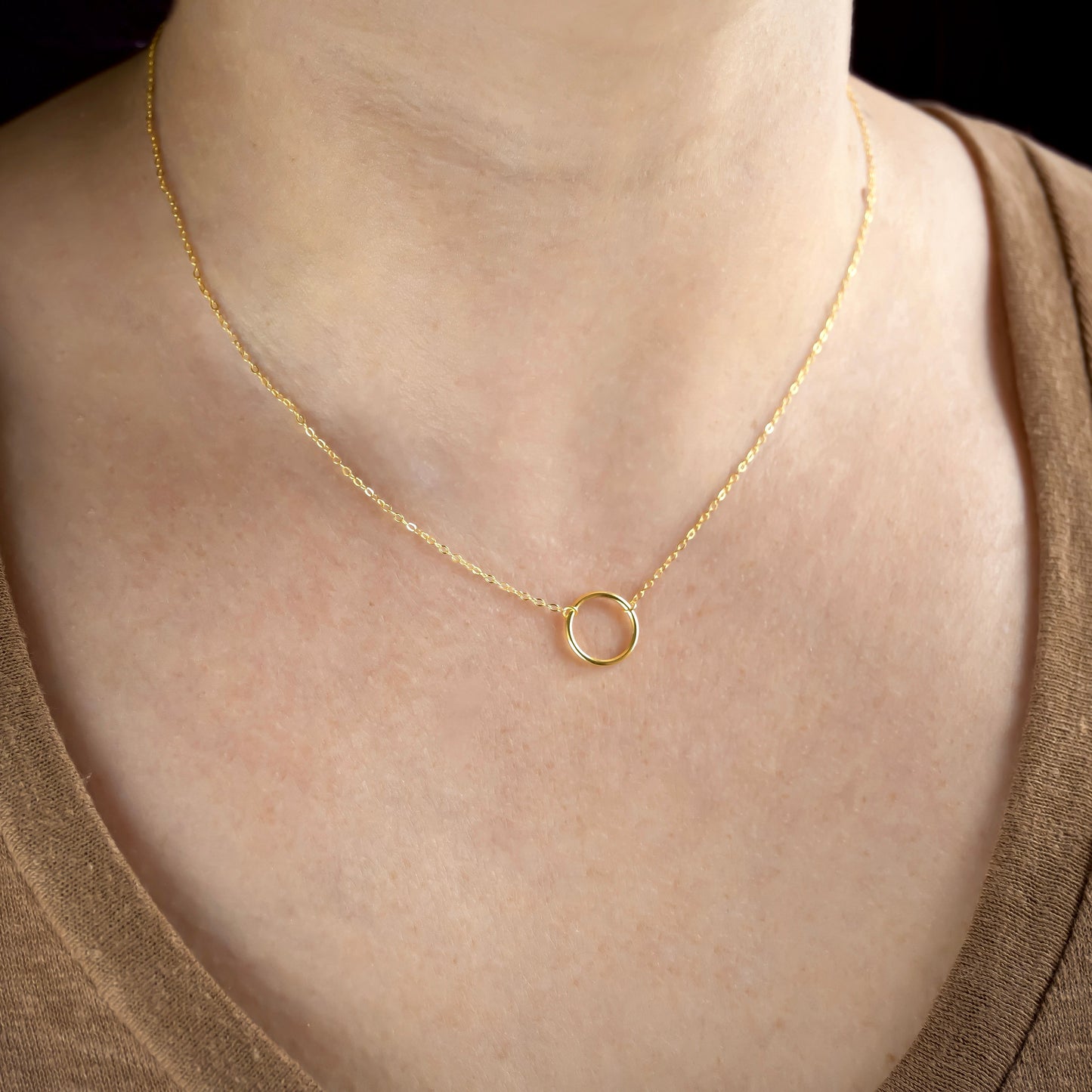 Gold necklace with a small ring pendant on a person wearing a brown top.