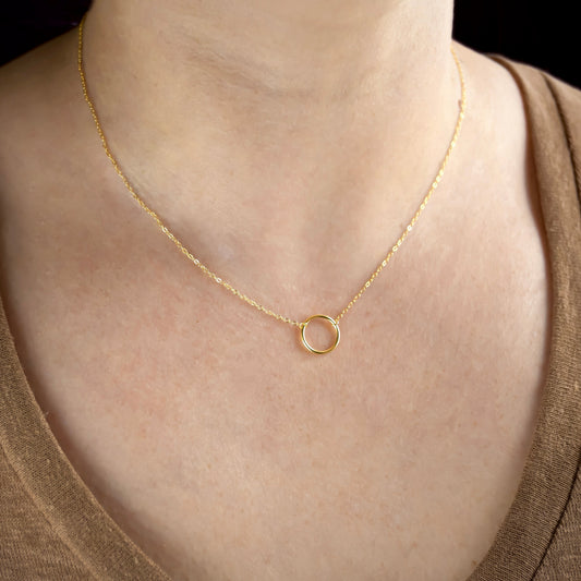 Gold necklace with a small ring pendant on a person wearing a brown top.