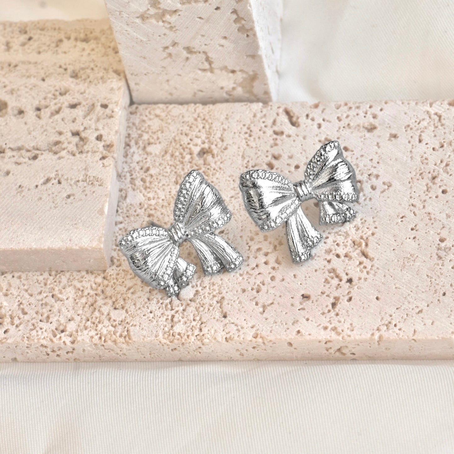 Silver ribbon earrings on a textured beige surface