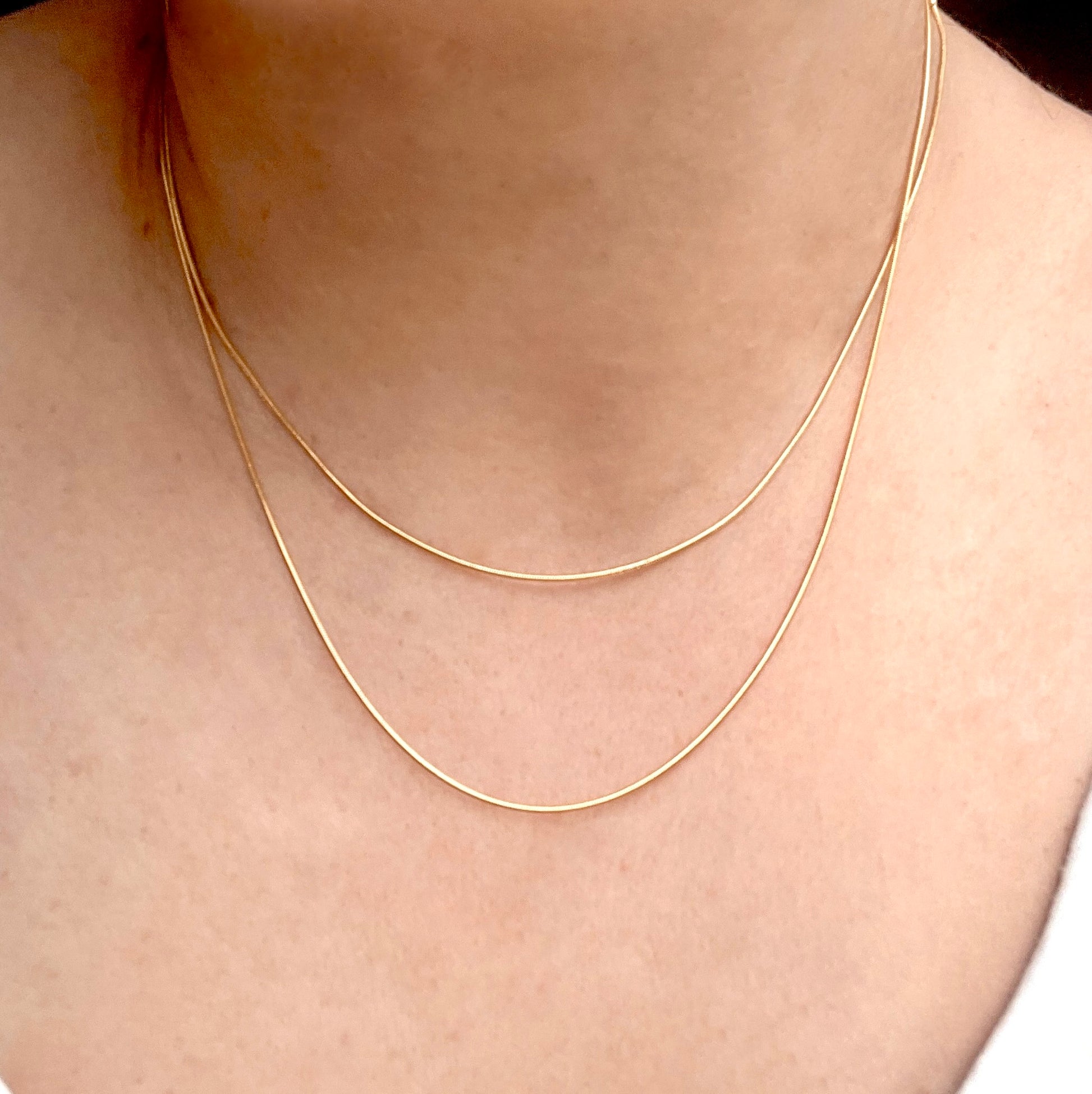 Gold layered snake chain necklace on a person's neck with a plain background